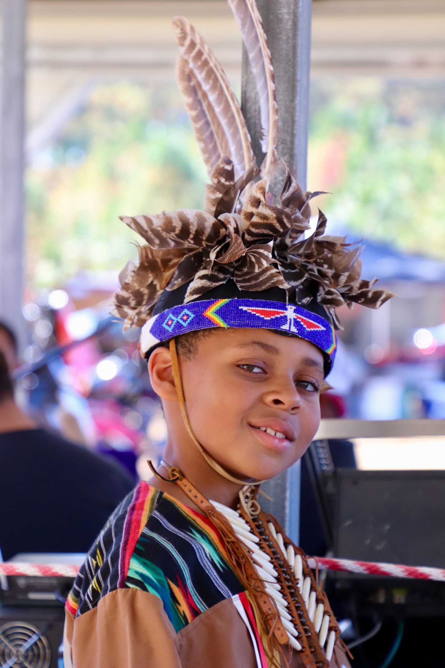 Young boy wearing traditional Native American regalia with feather headdress at a cultural event in North Carolina.