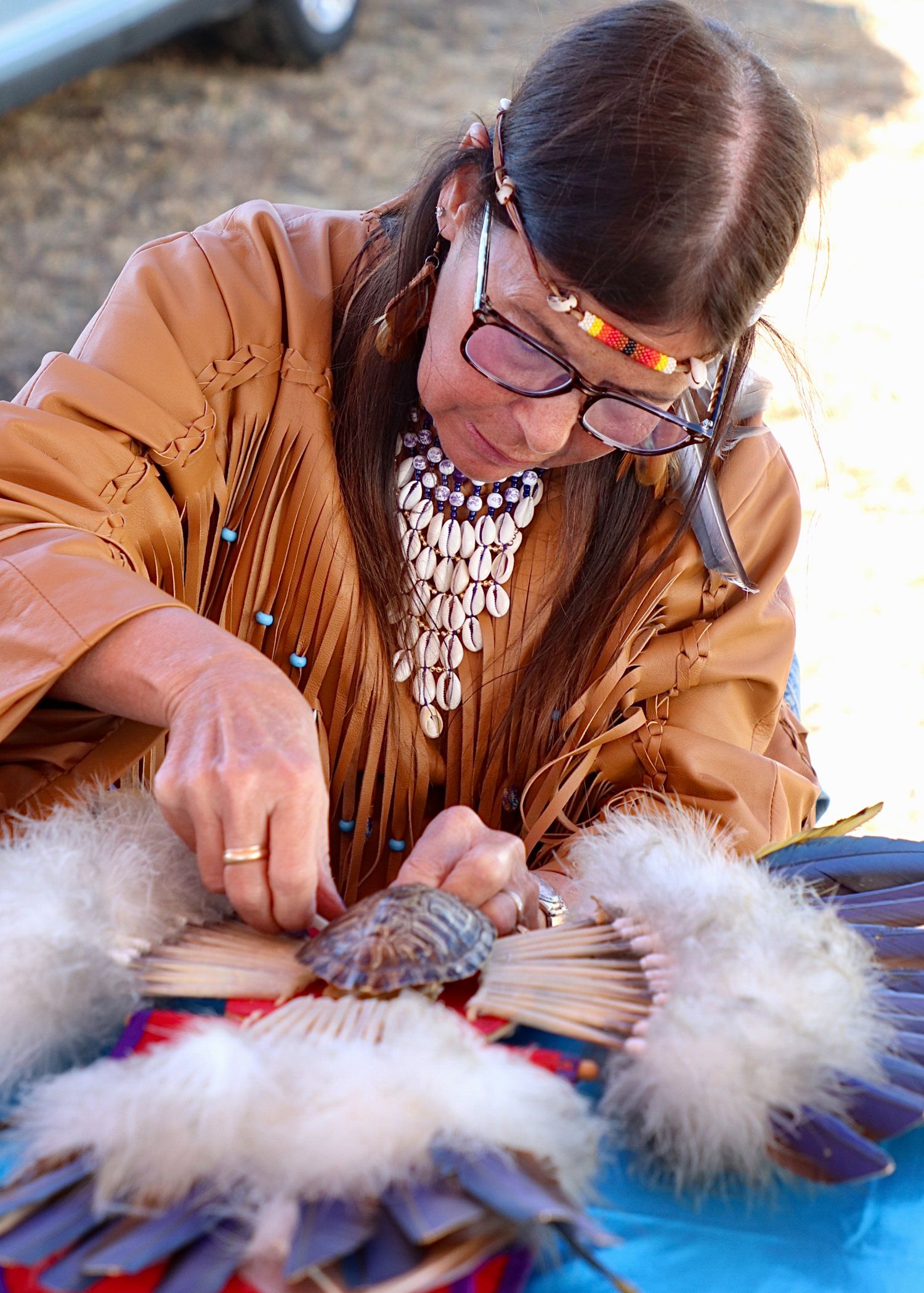 Native American woman in traditional dress creating a handmade feather fan at a cultural gathering.