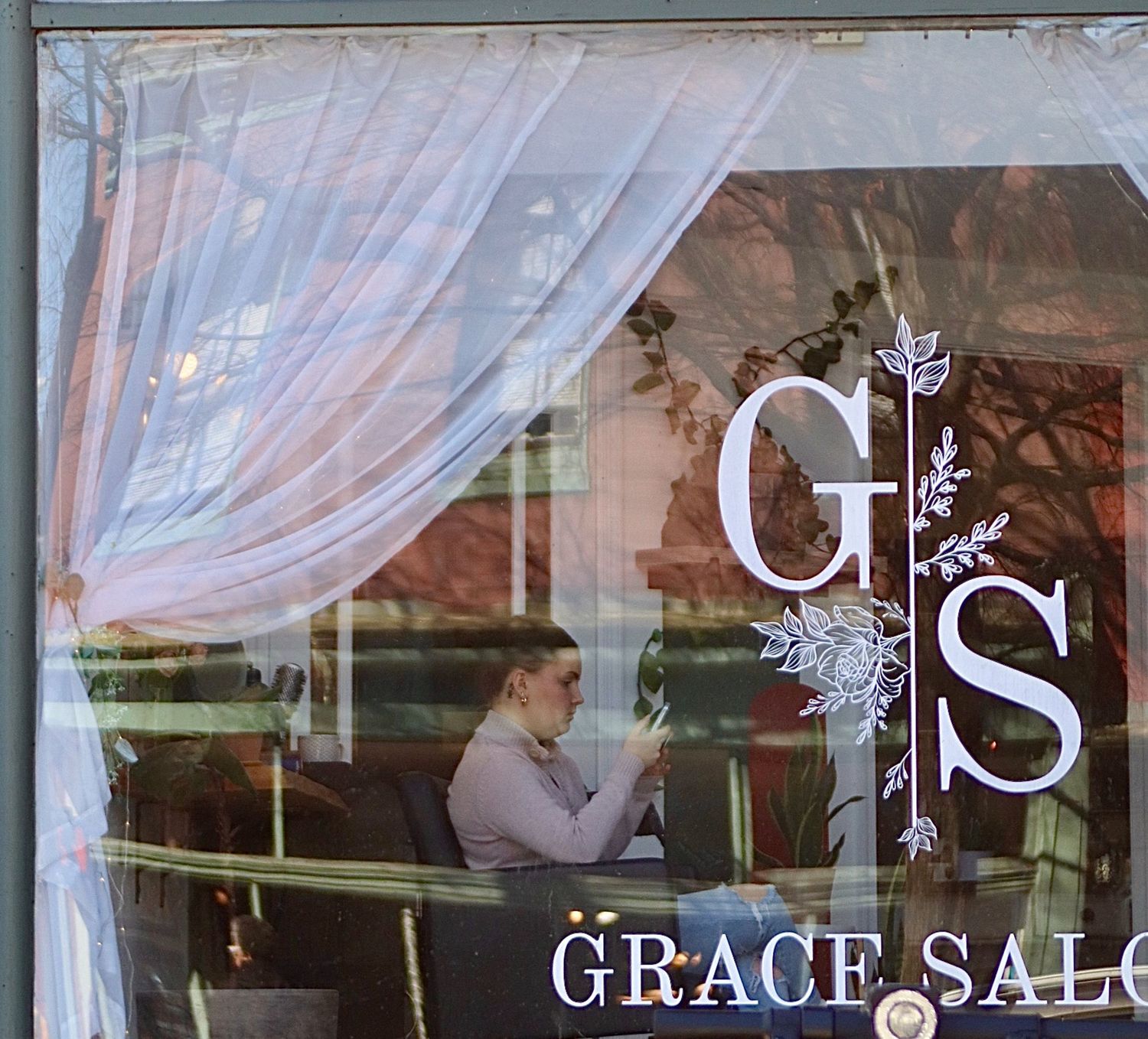 A sheer white curtain hangs in front of a window with 'GS Grace Salon' lettering visible through the fabric.