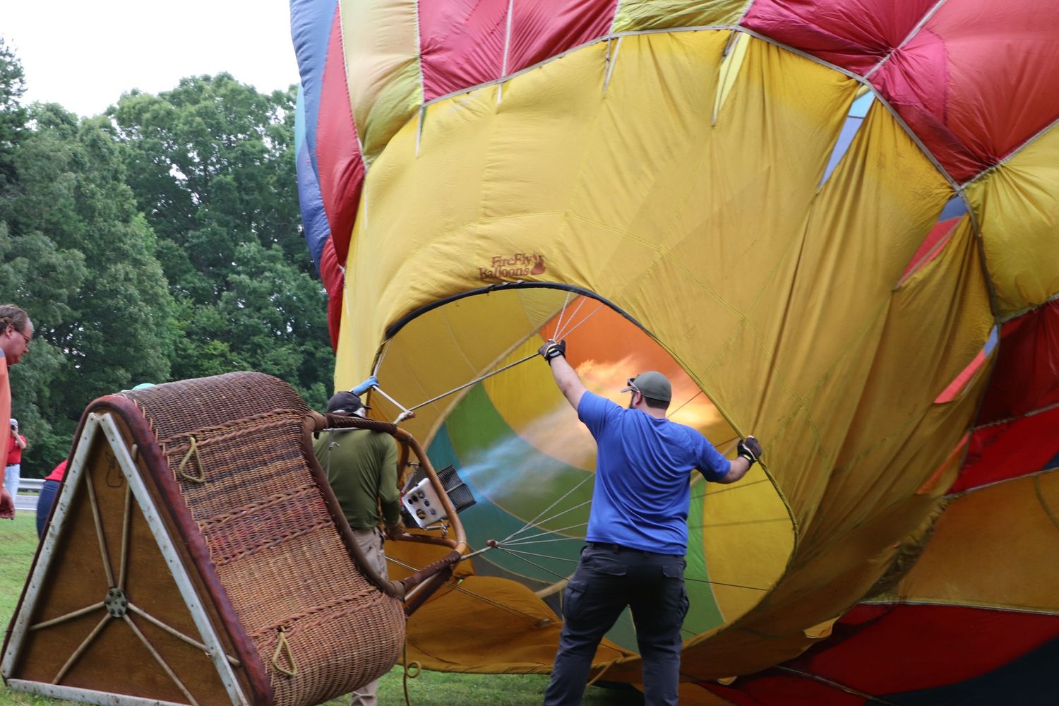 Crew members prepare a hot air balloon as flames fill the colorful fabric in an open field