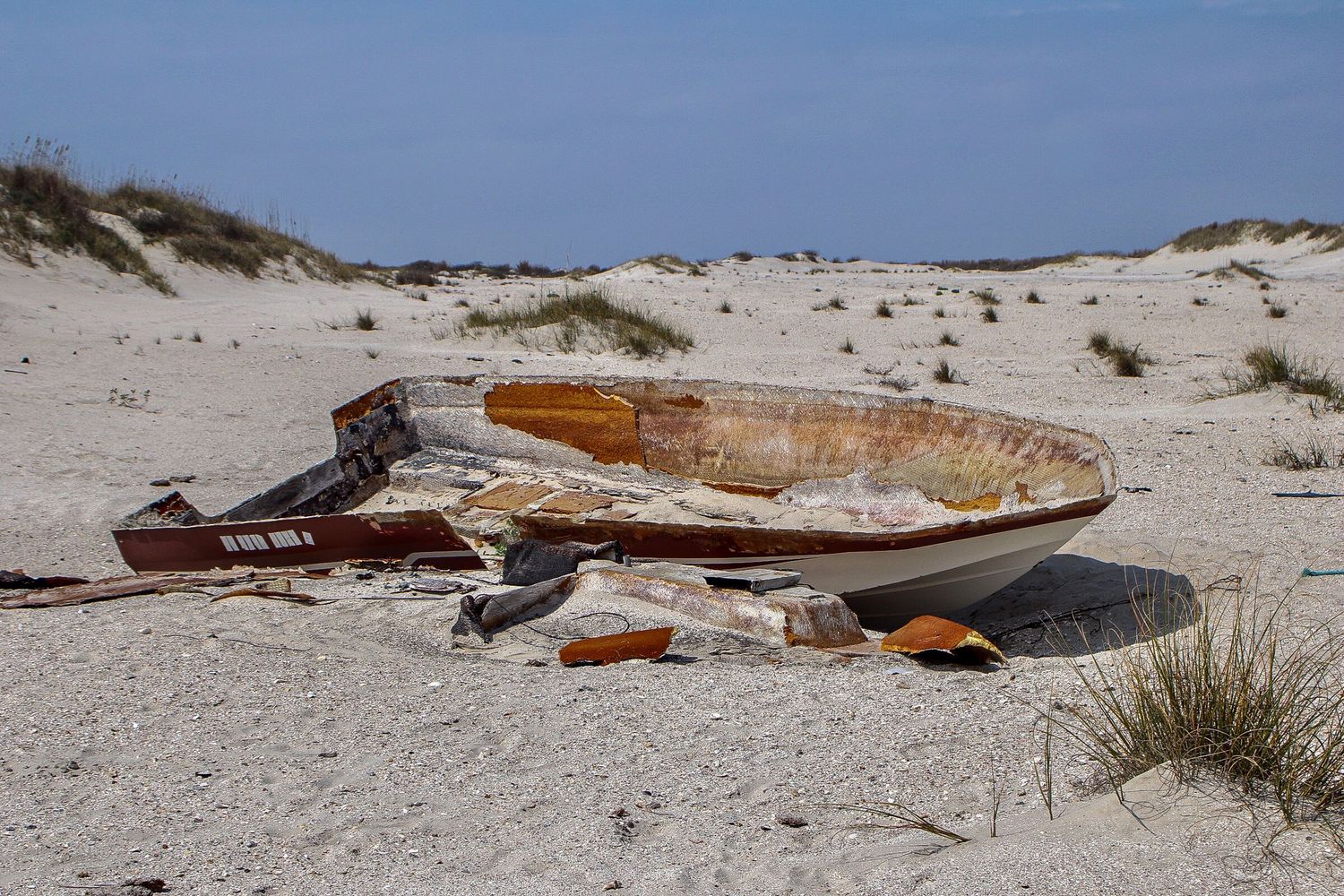 Abandoned and deteriorating boat hull resting on sandy coastal dunes.