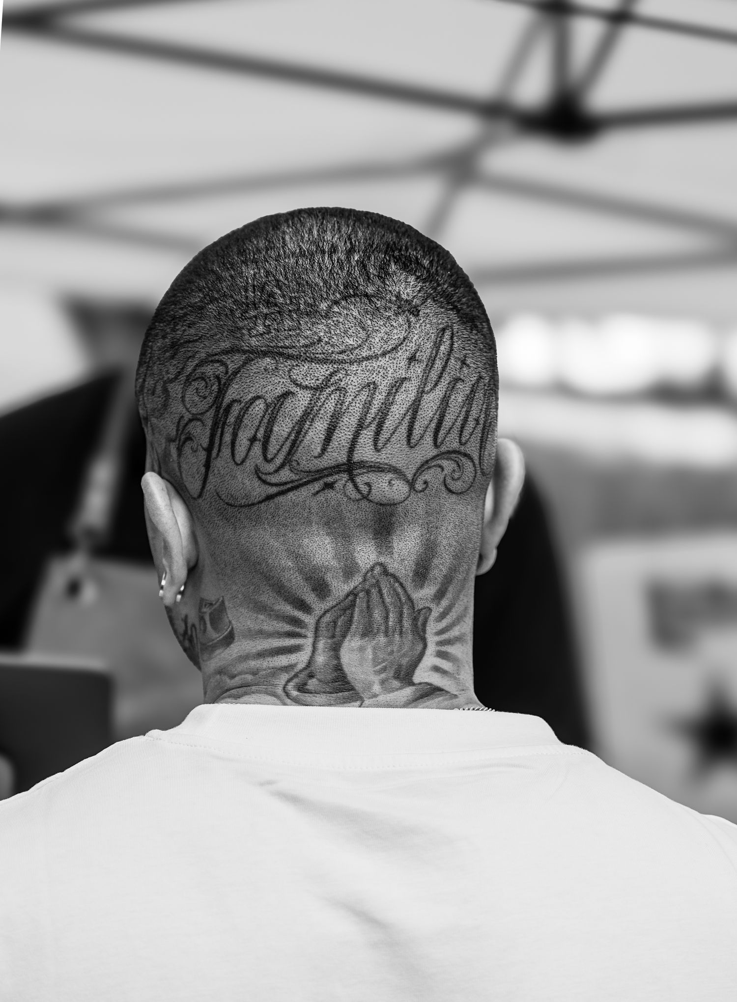 “Familia” and praying hands tattoos on the back of his head, reflecting identity and cultural values.