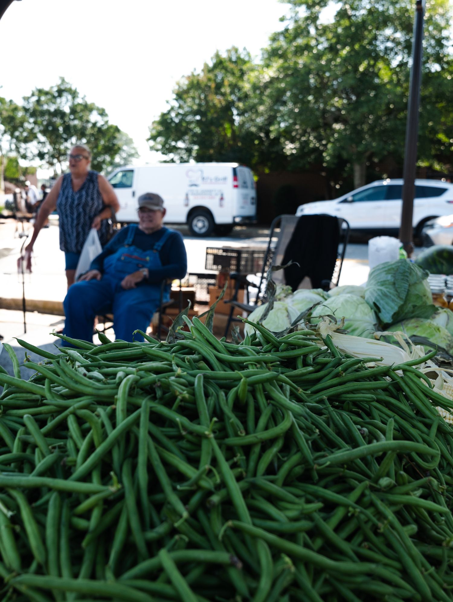 Fresh green beans piled at a farmers market with shoppers in the background in a small Texas town.