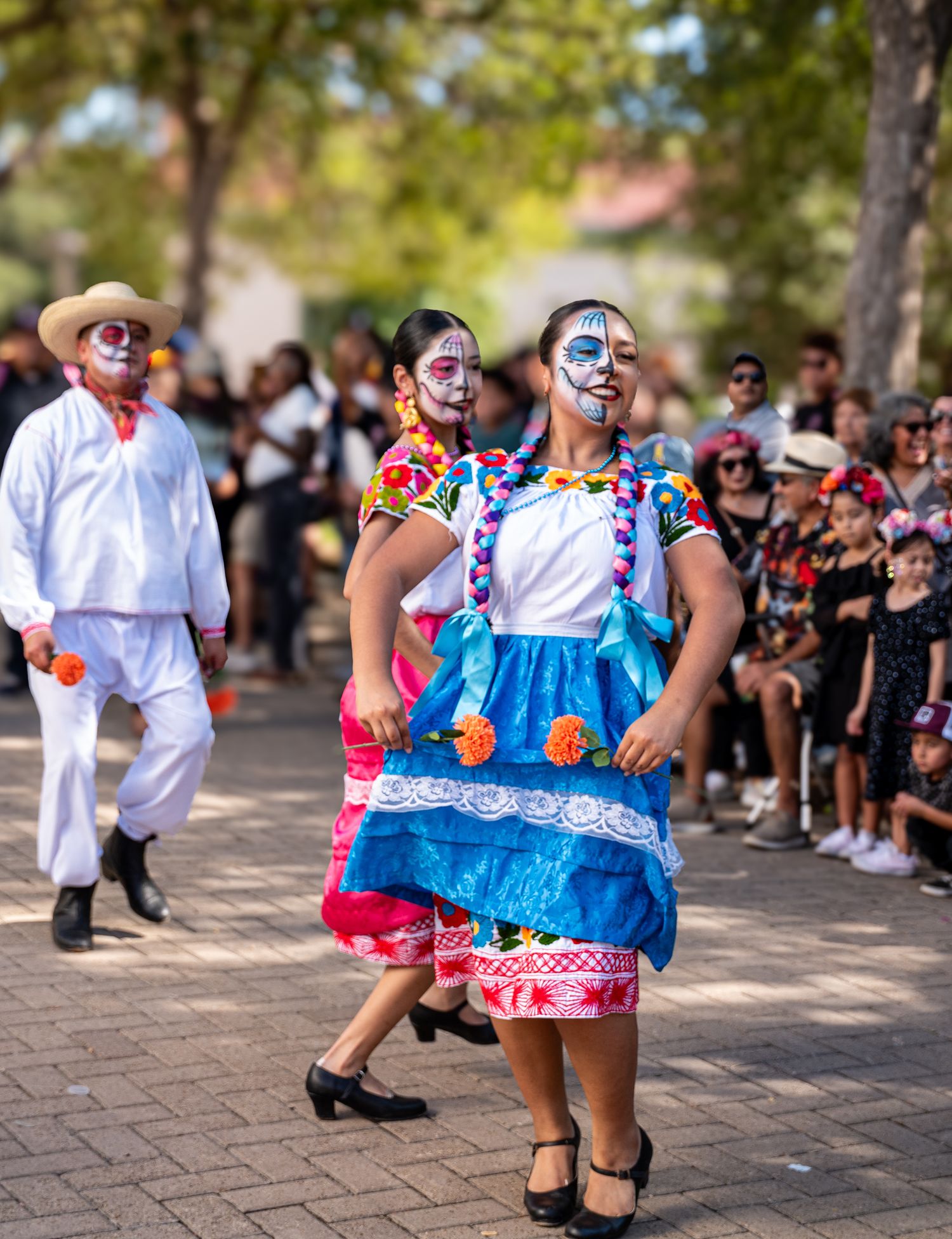 Dancers in traditional Mexican Day of the Dead costumes with face paint performing in a cultural parade.