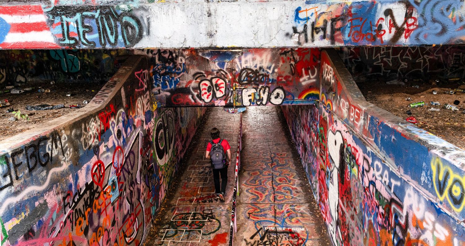 Person walking through a graffiti-covered underpass, surrounded by colorful street art.