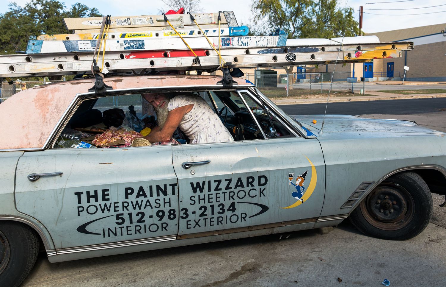 A man inside a work car carrying tools and belongings, capturing a moment of daily life and survival in a small Texas town.