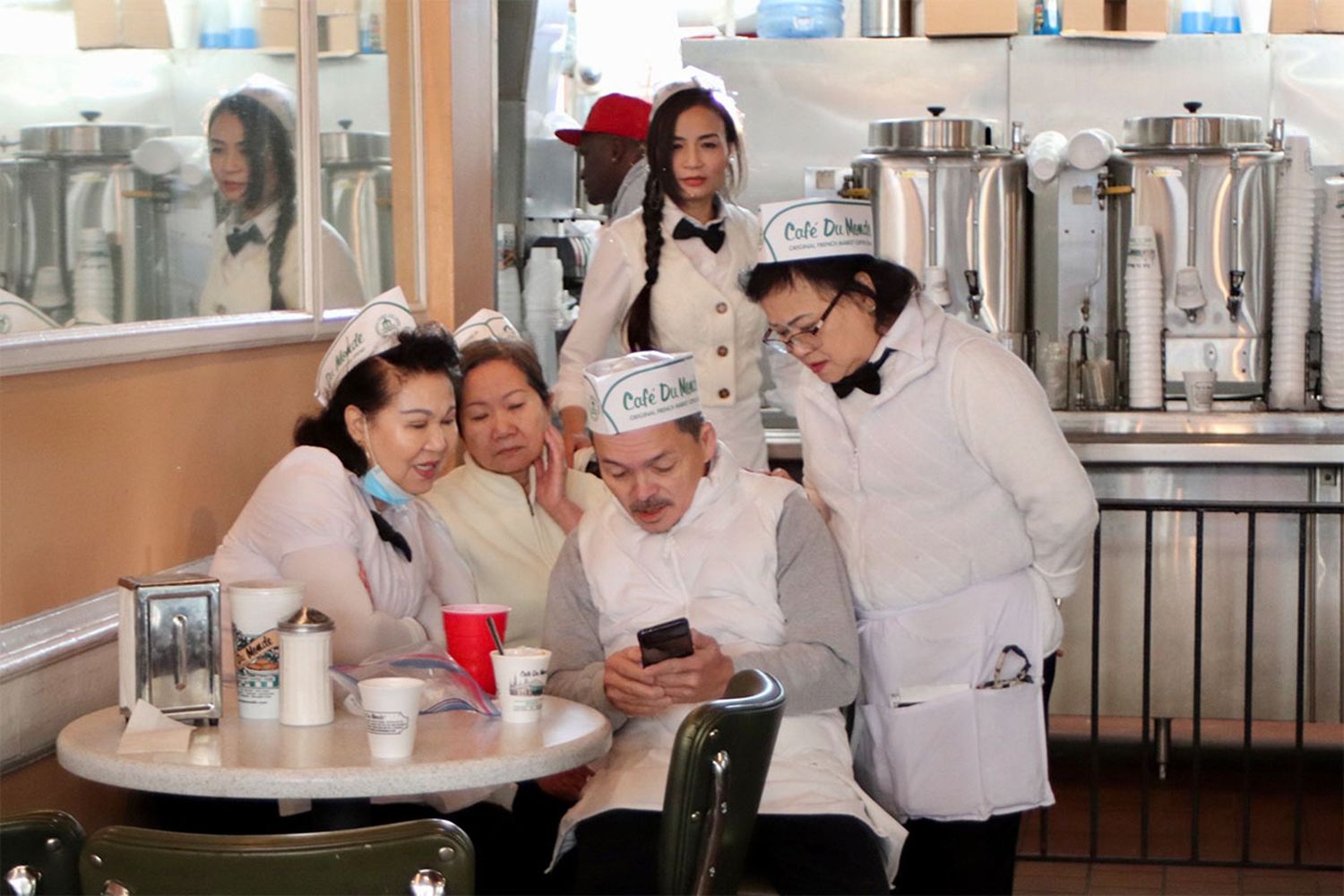 Café Du Monde workers gathered around a table looking at a phone inside the New Orleans café.