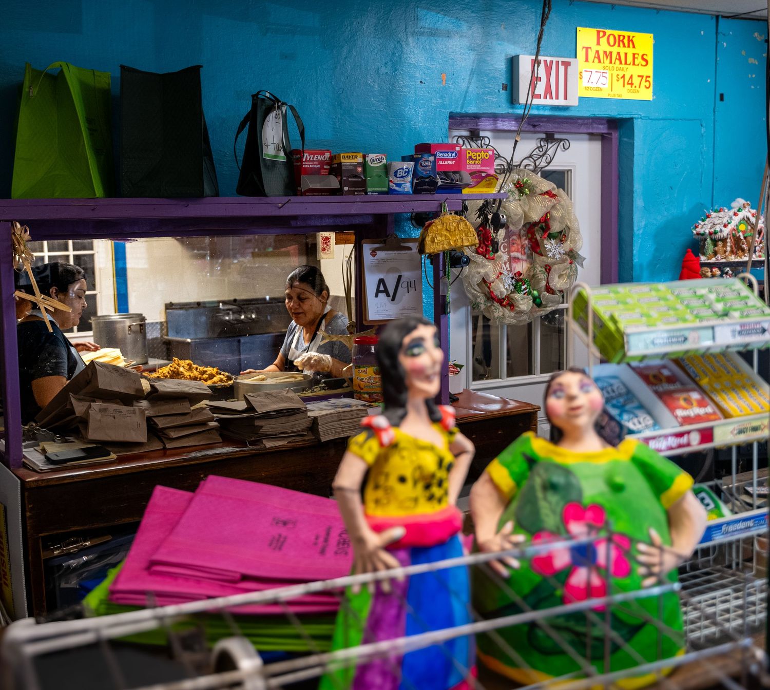 Women preparing pork tamales behind a counter inside a small Hispanic grocery store.
