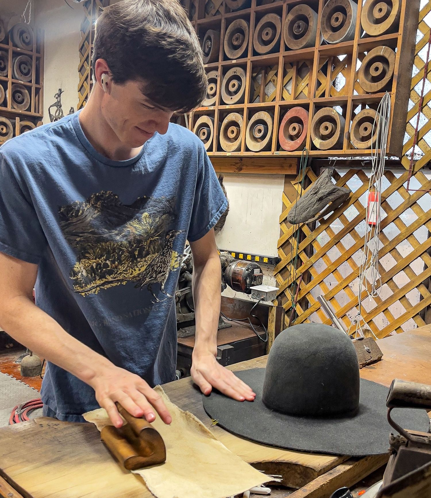 A craftsperson carefully shapes and molds a black felt hat using traditional hat-making tools and techniques.