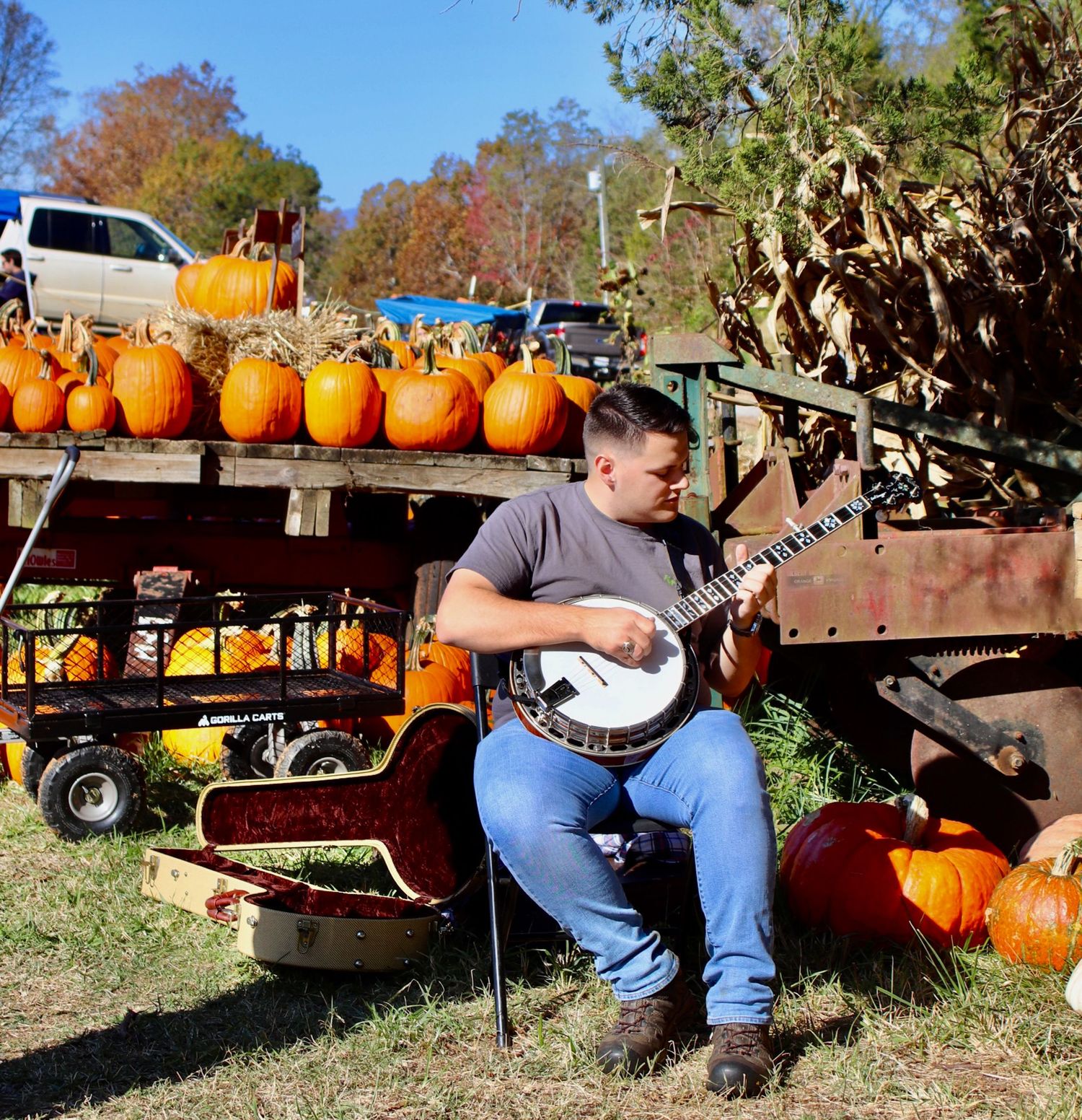 Man playing banjo beside pumpkins at a fall market in a rural North Carolina setting.
