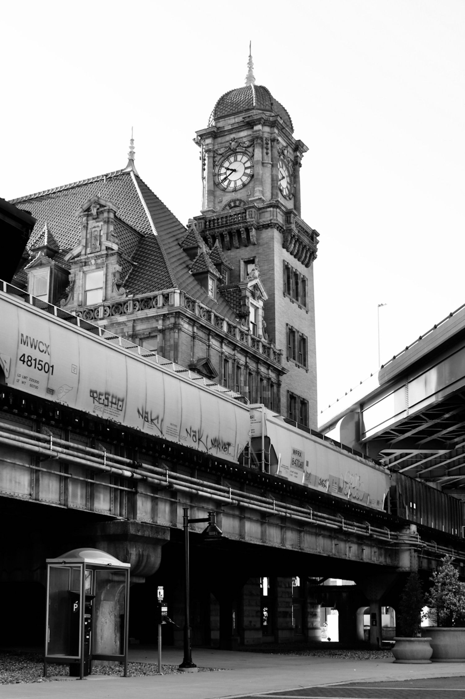 Historic clock tower building behind a freight train on elevated tracks in a Virginia city, shown in black and white.
