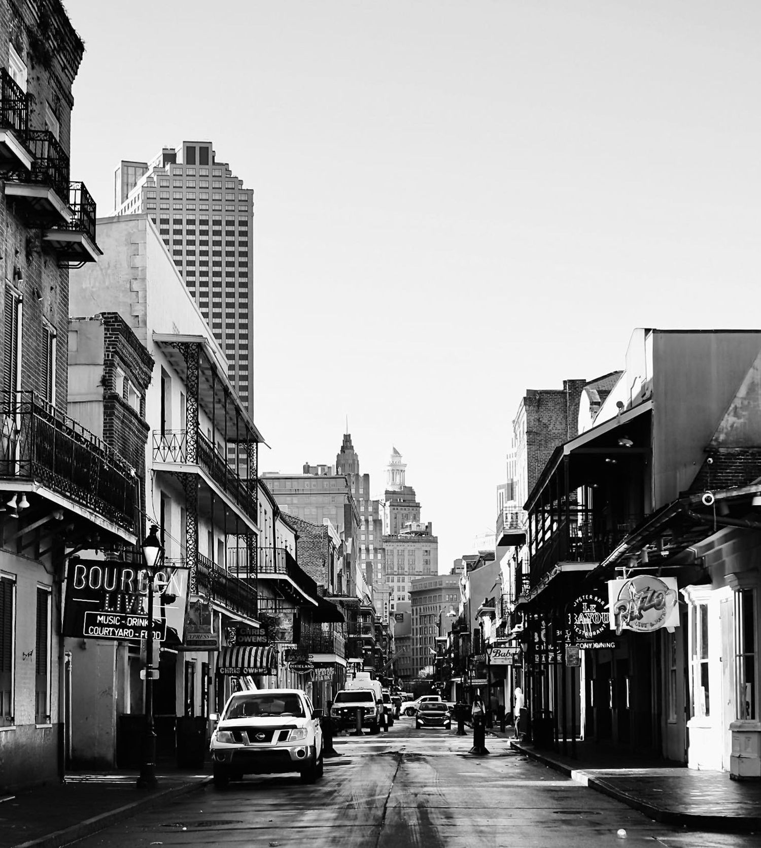 Street view of historic buildings and storefronts in a New Orleans city scene, shown in black and white.