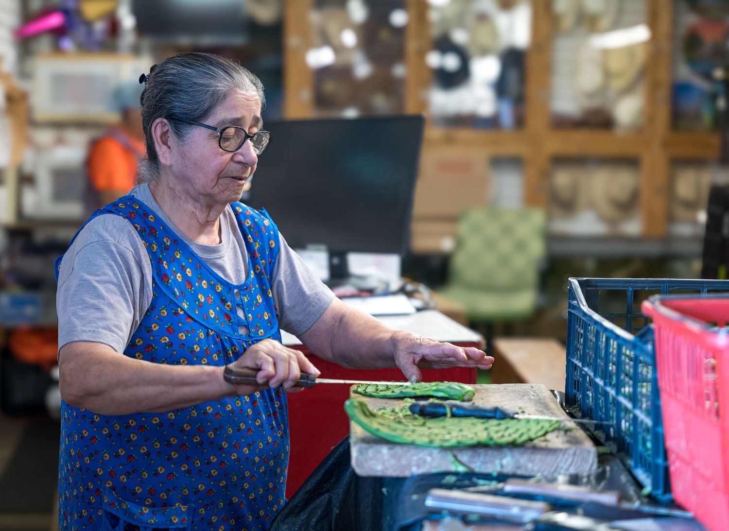 Woman preparing nopales on a cutting board inside a small Hispanic market.