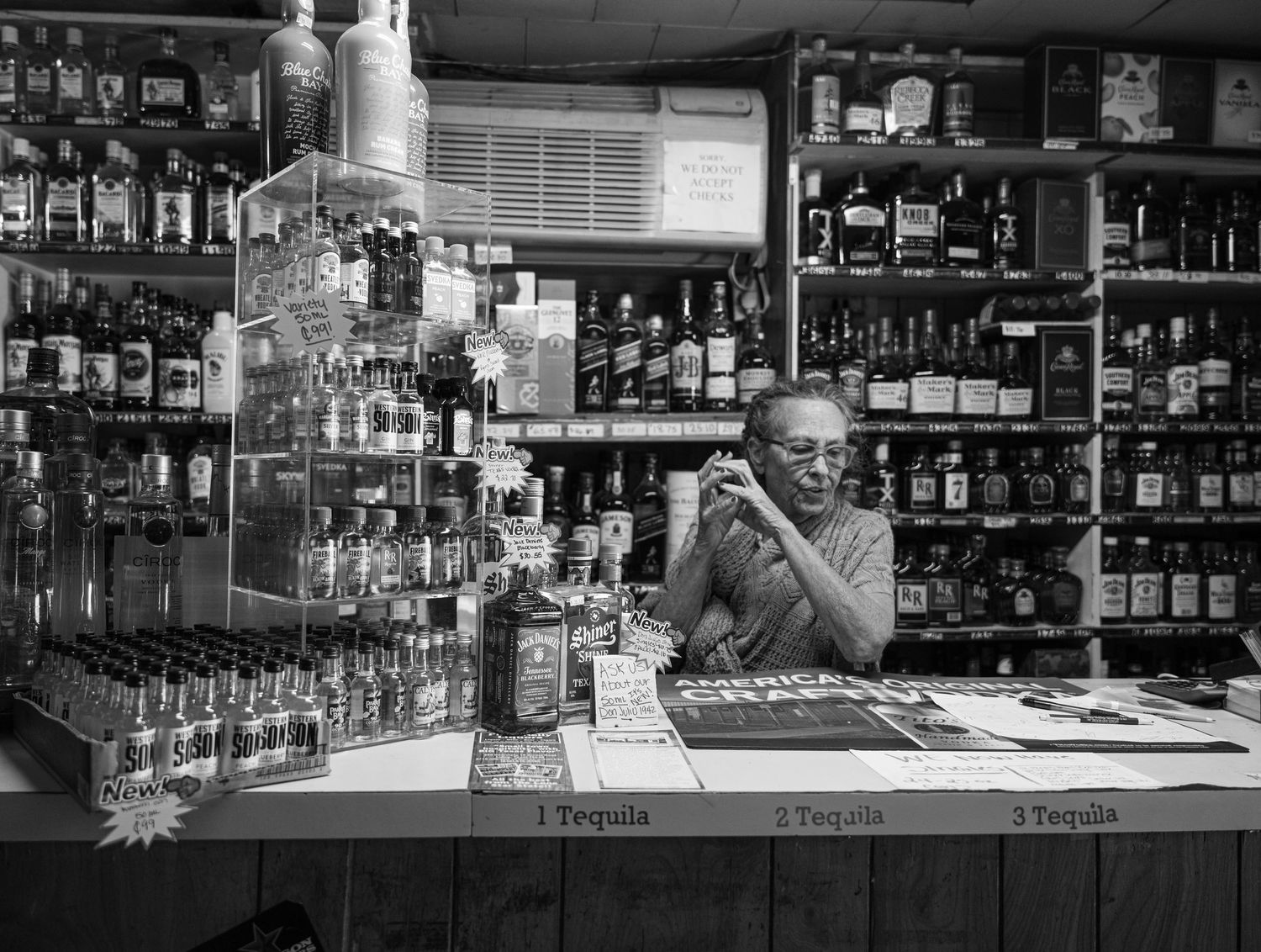 Black and white photo of historic Texas liquor store counter with shelves of bottles and someone working behind the bar.