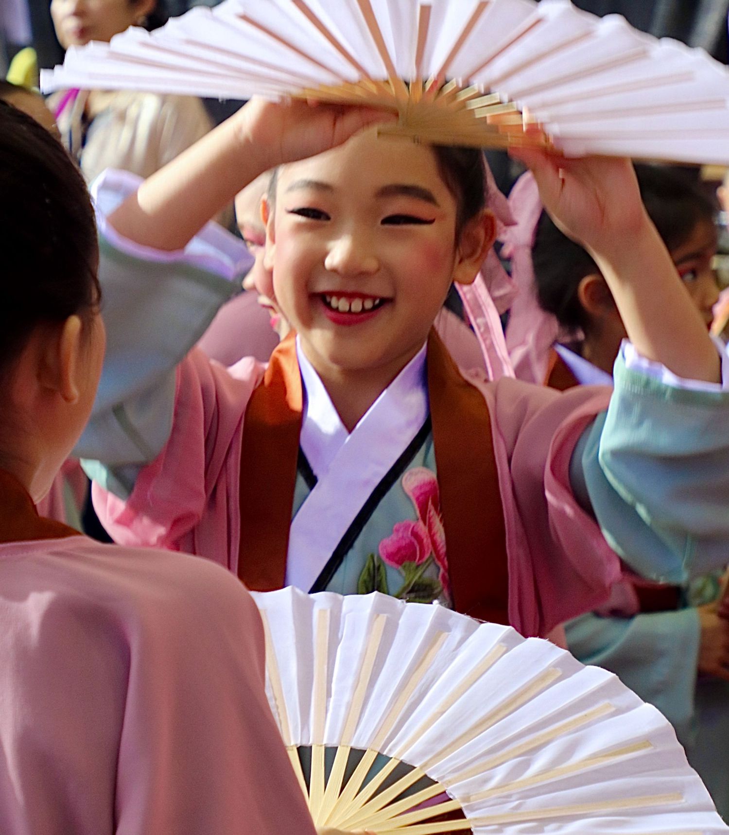 Young girl in traditional Korean hanbok smiling while holding a folding fan during a cultural dance performance.