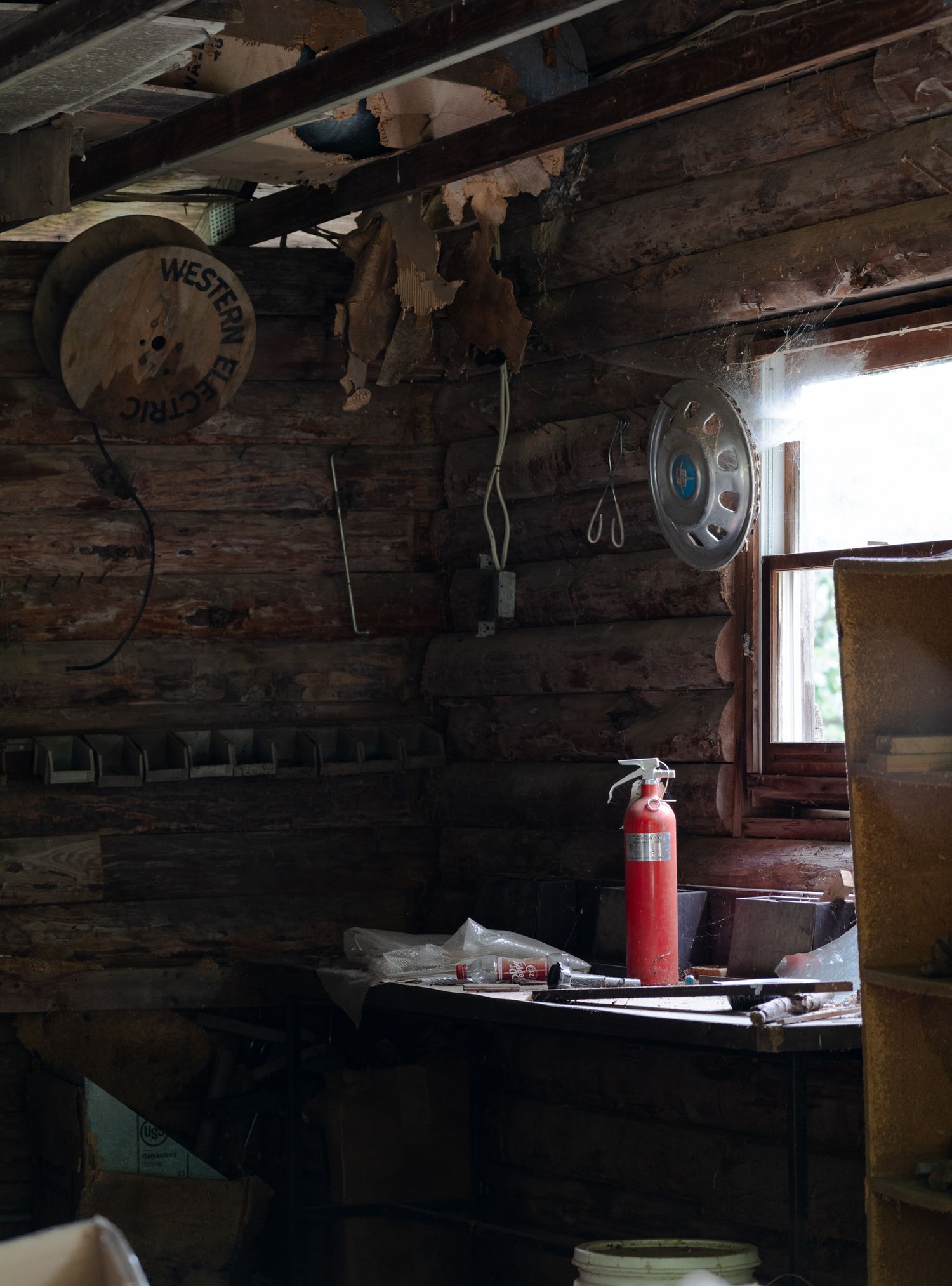 An abandoned or aging workshop interior with worn wood walls, tools, and light filtering through a small window.