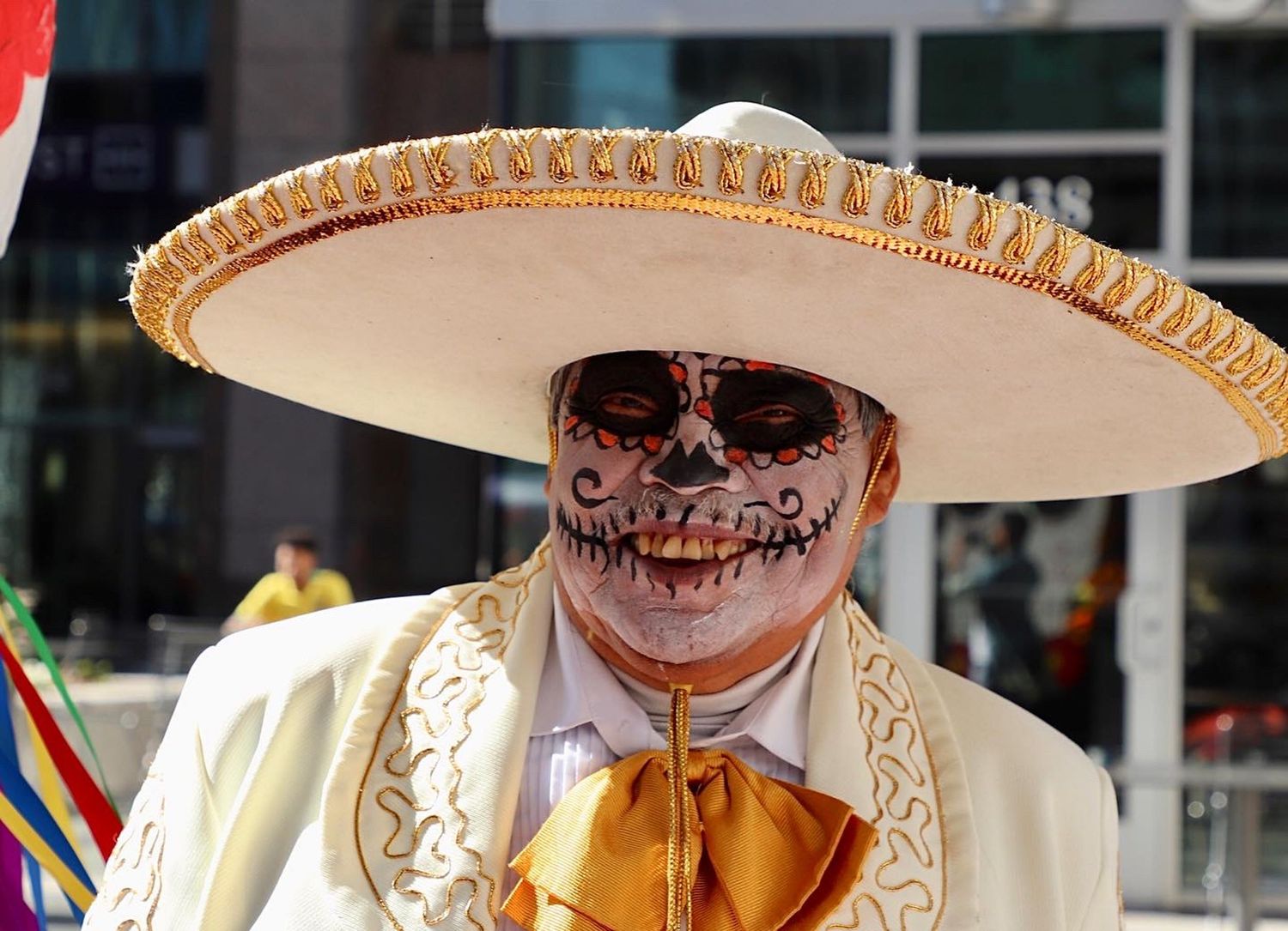 Man in traditional charro suit and sombrero with Día de los Muertos face paint smiling at a cultural celebration.