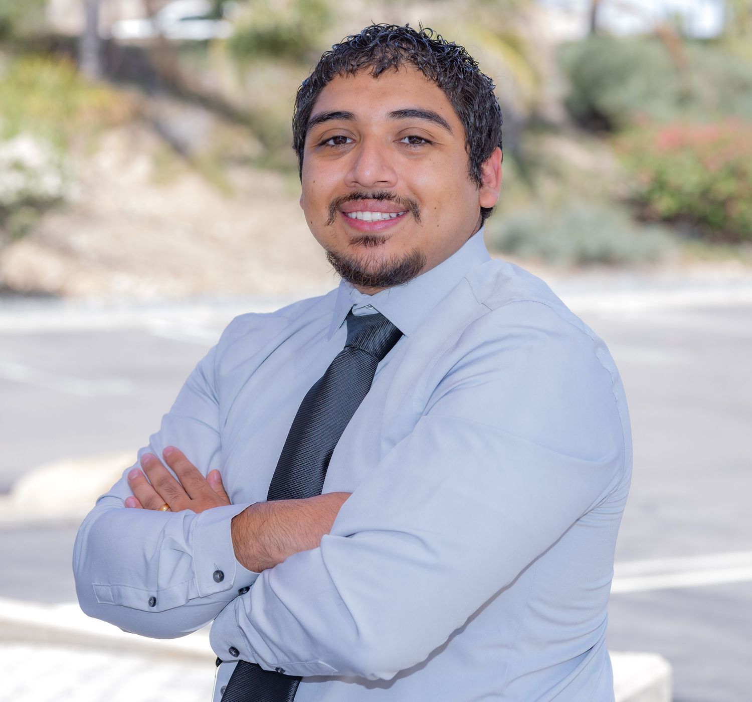 Professional outdoor headshot of a man wearing a dress shirt and tie with his arms crossed.