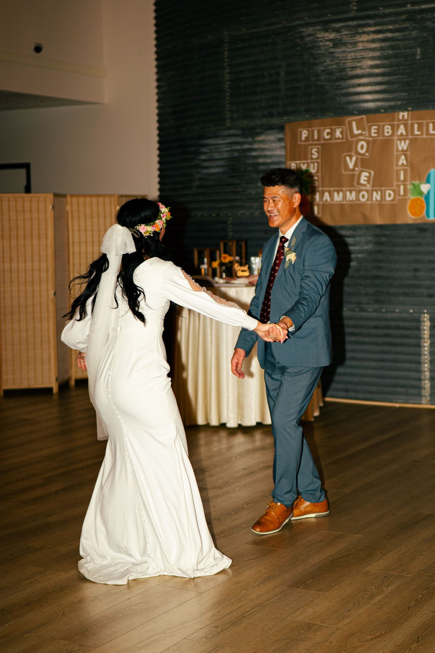 Bride and groom share joyful first dance at wedding reception with decorative letter board in background.