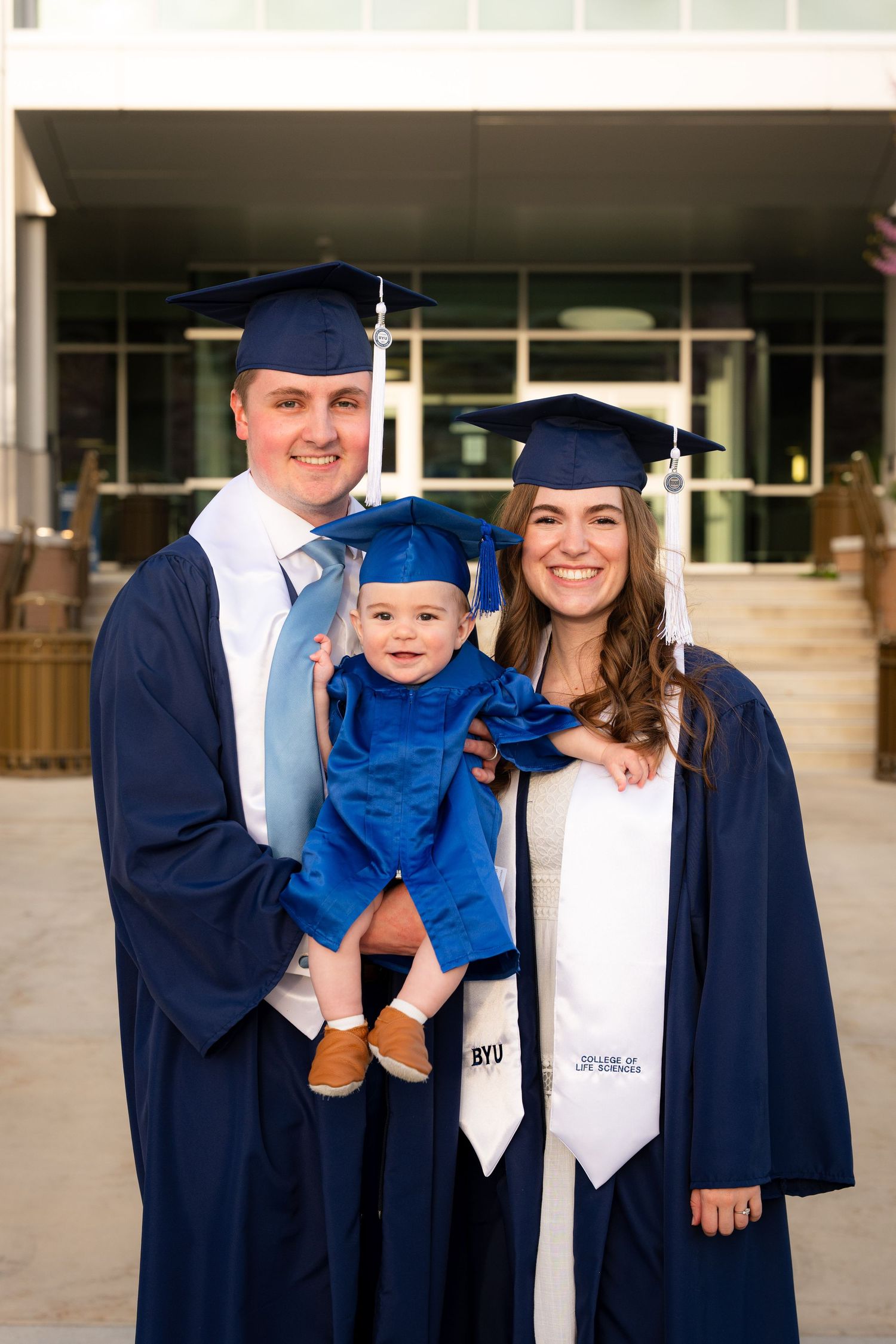 A family, including a woman, man, and baby, stand together in front of a university building.