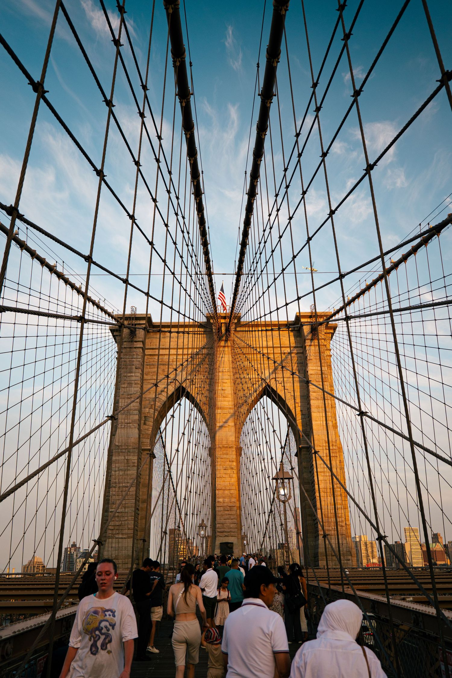 The image shows the iconic Brooklyn Bridge in New York City, with its intricate web of cables and towers against a blue sky.