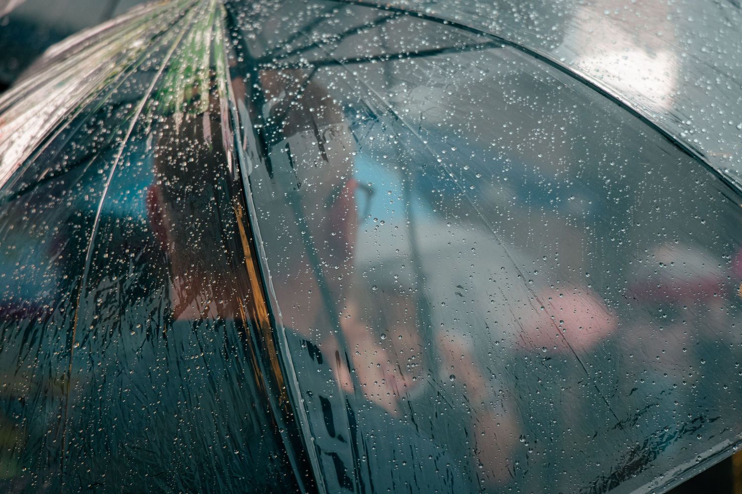 Close-up of raindrops on a transparent umbrella, with a blurred cityscape in the background.