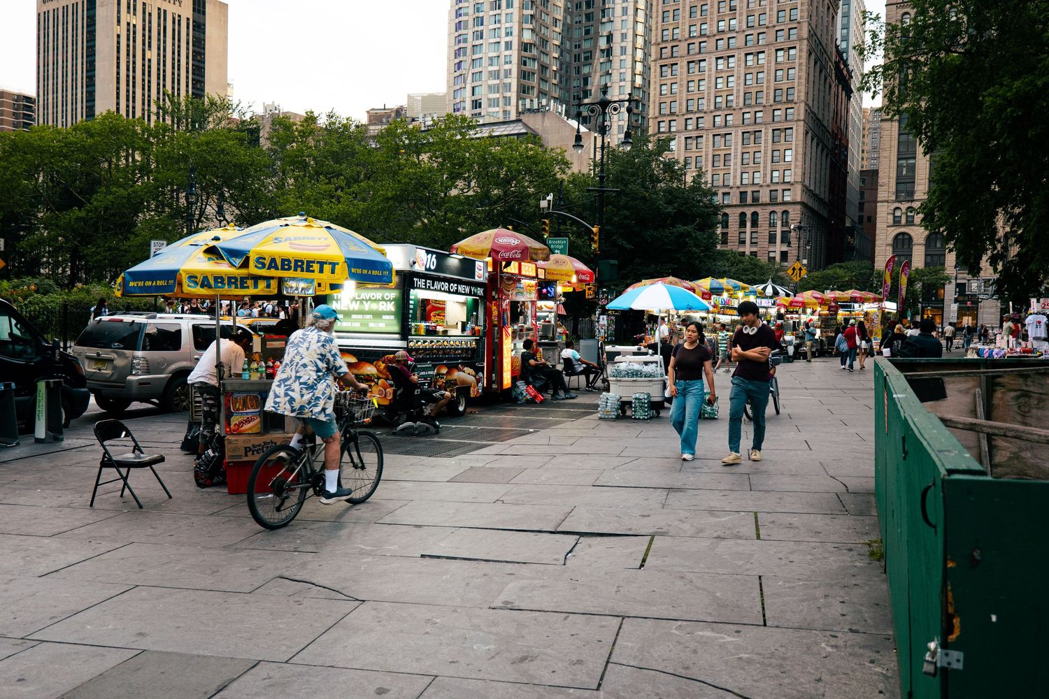 The image shows a bustling street scene in New York City, with various food and merchandise vendors set up along the sidewalk.