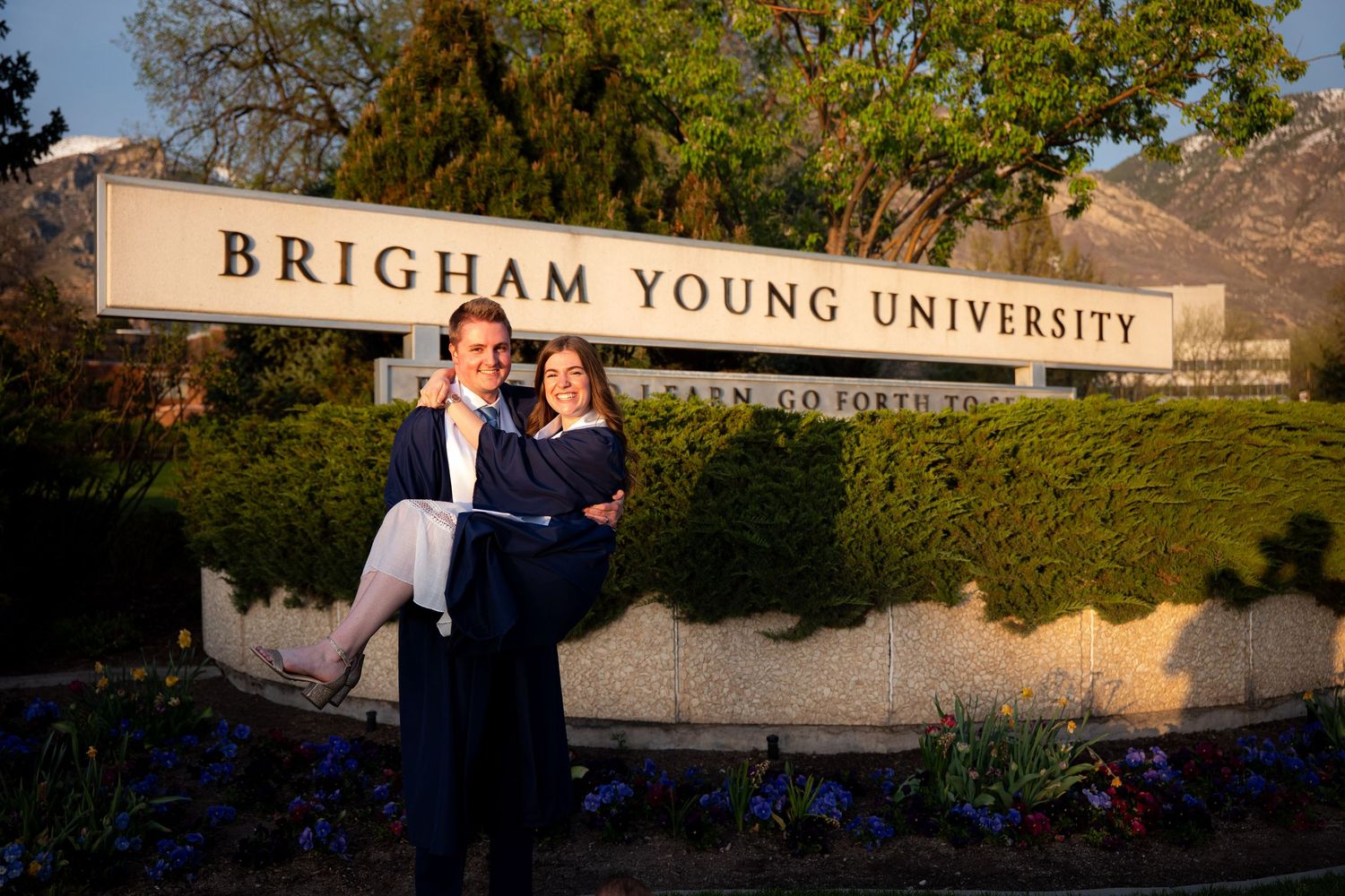 A couple is posing for a photo in front of a sign for Brigham Young University.