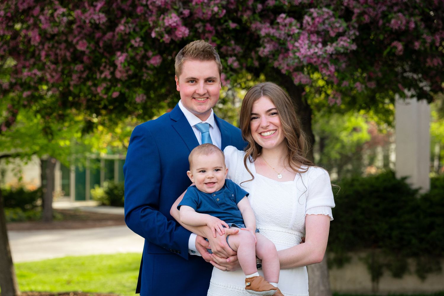 A happy family portrait of a couple and their young baby in a scenic outdoor setting.