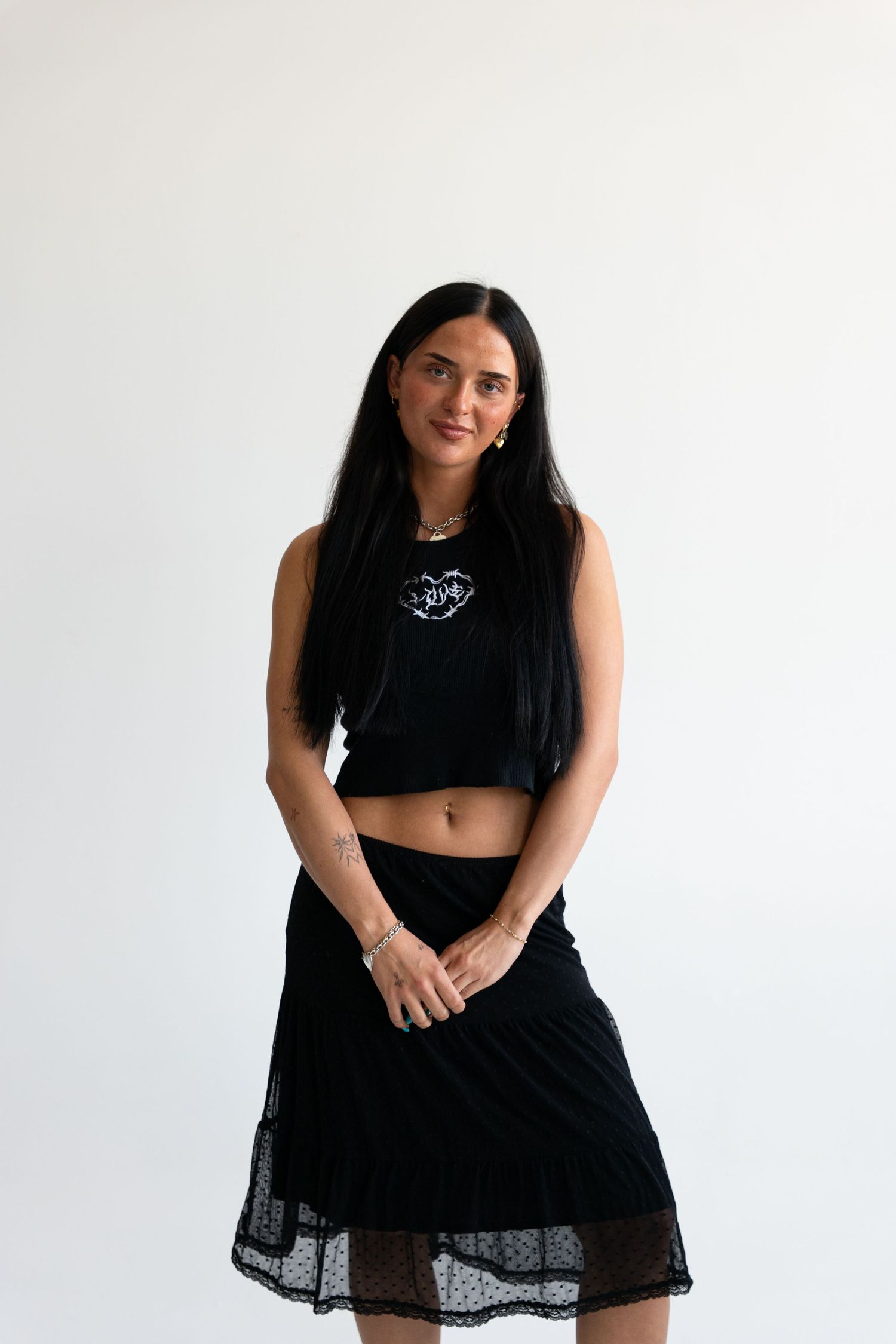 Woman in black crop top and midi skirt posing against white background.