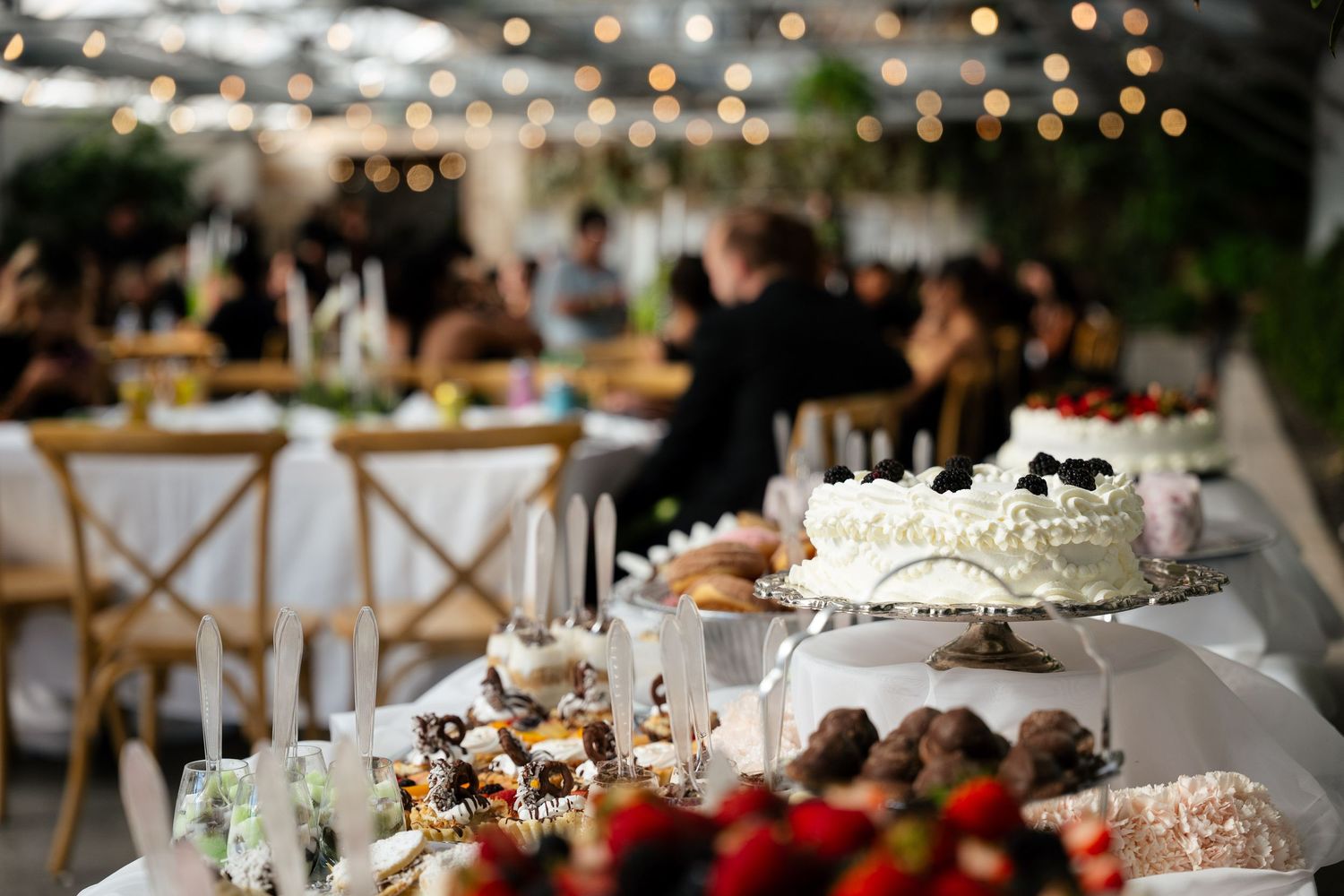 Elegant dessert table with white cake, strawberries, and chocolates at a candlelit indoor wedding reception.