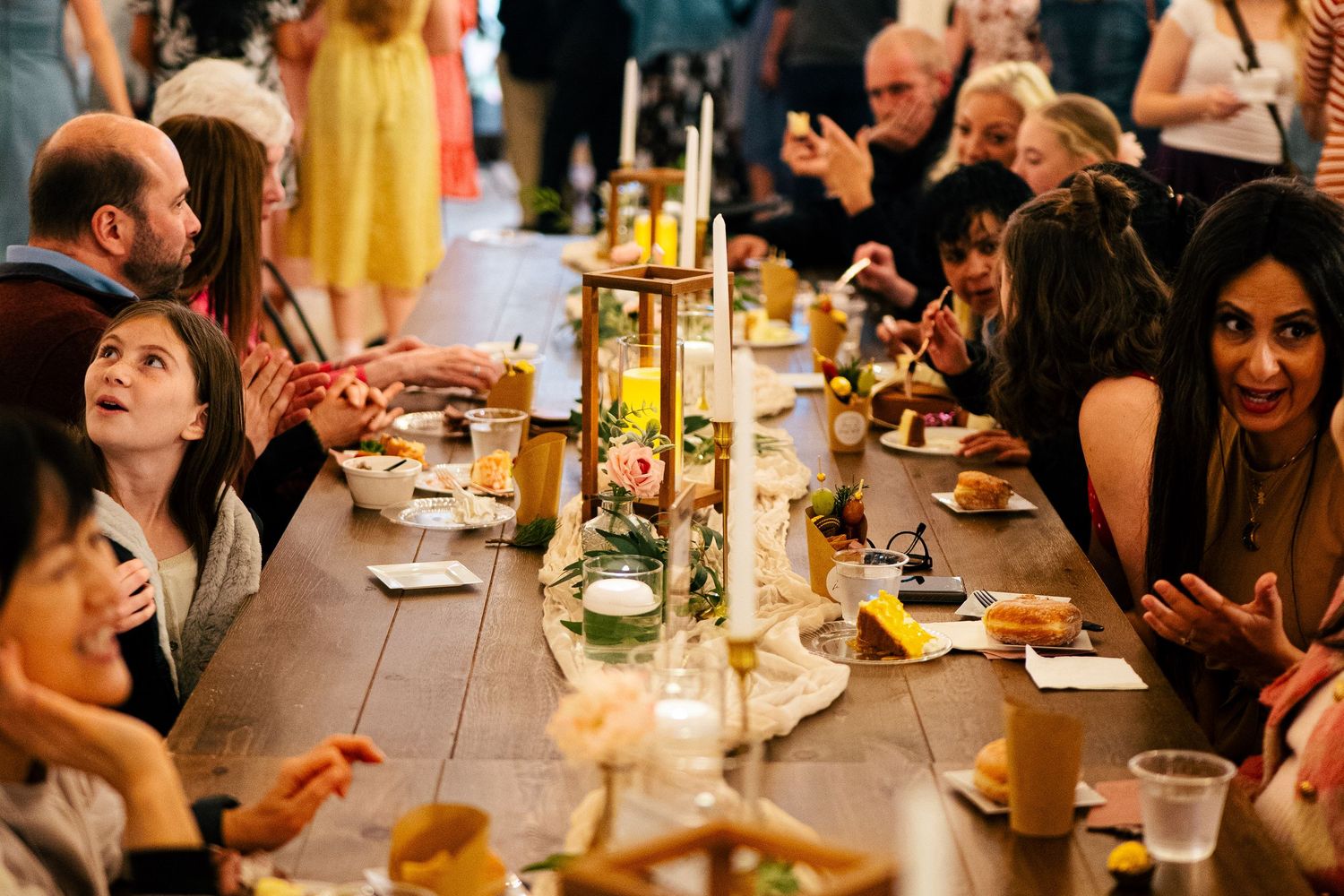 Guests gathered around a rustic wooden dining table with candles and floral centerpieces at an elegant dinner event.