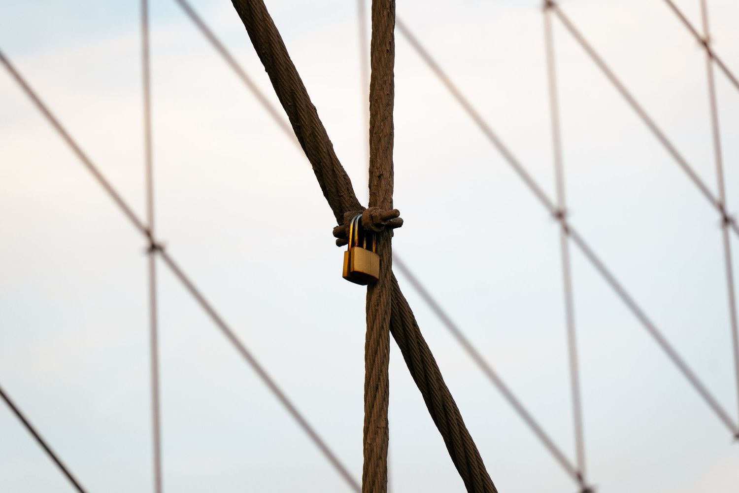 Close-up of the metal cables and supports of a bridge, creating an abstract geometric pattern against the sky.