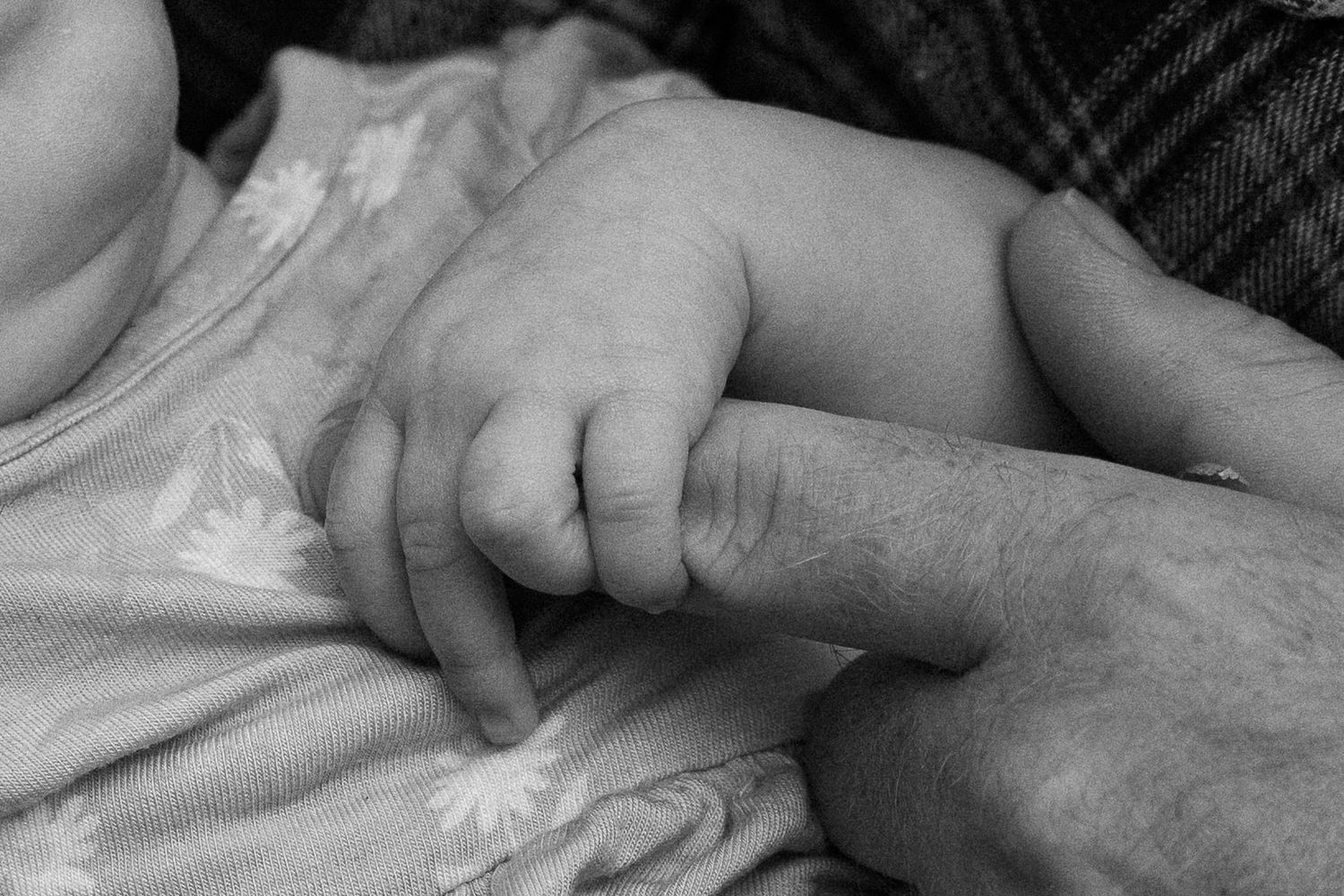Black and white photo of a newborn baby grasping an adult finger, symbolizing new life and family bond.