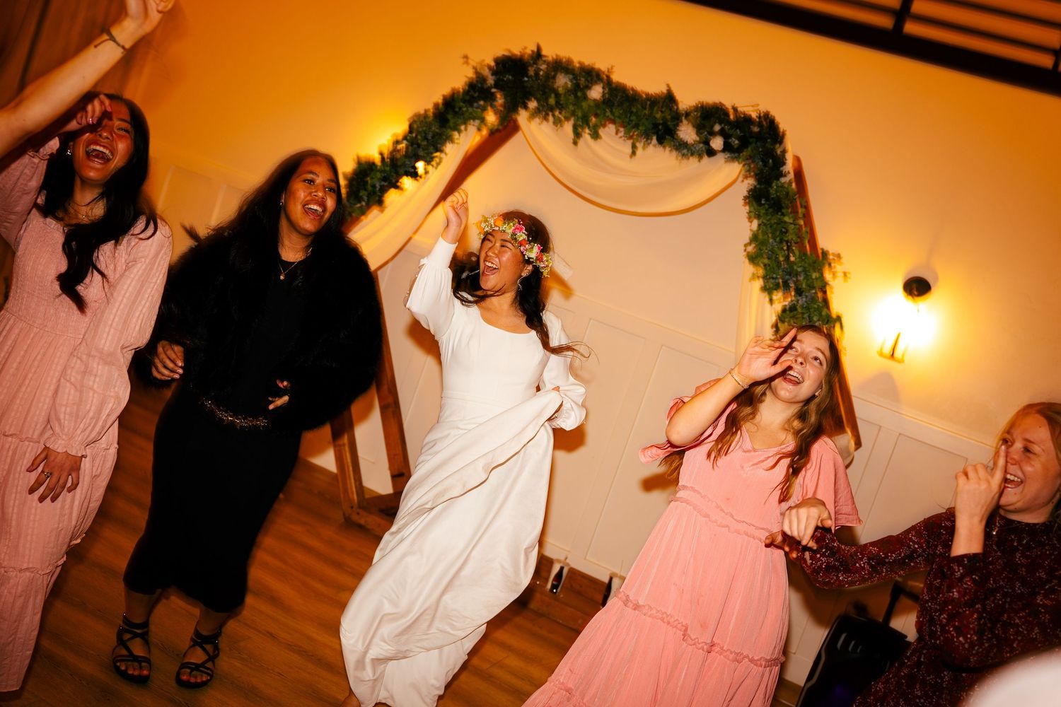 Bride in white gown dancing joyfully with guests at wedding reception.