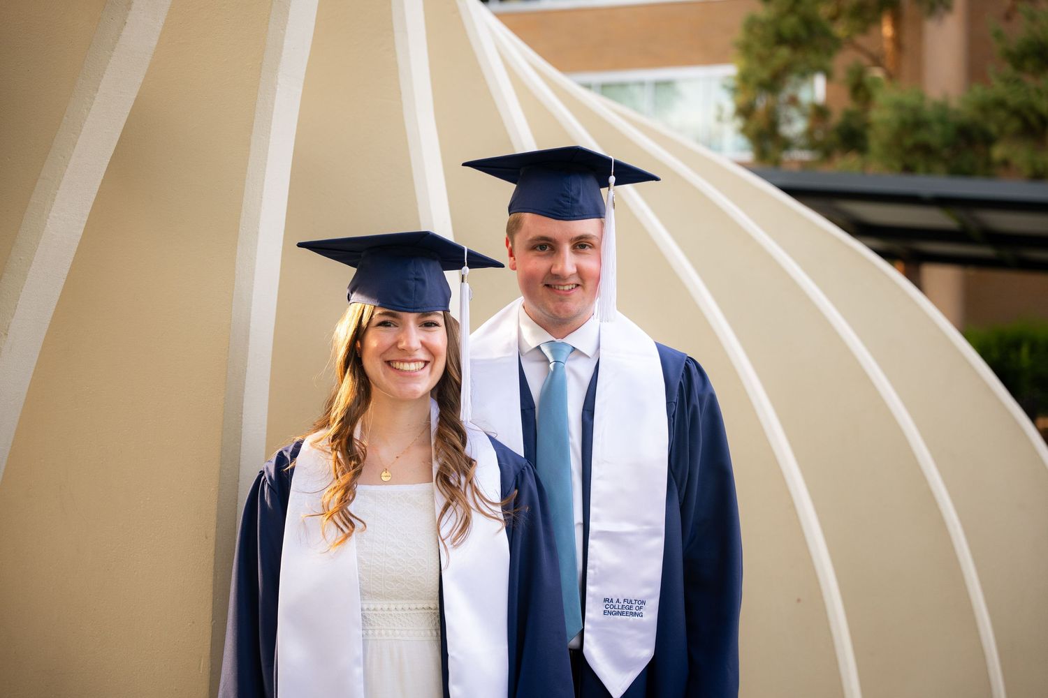 Two graduates in caps and gowns stand together and smile.