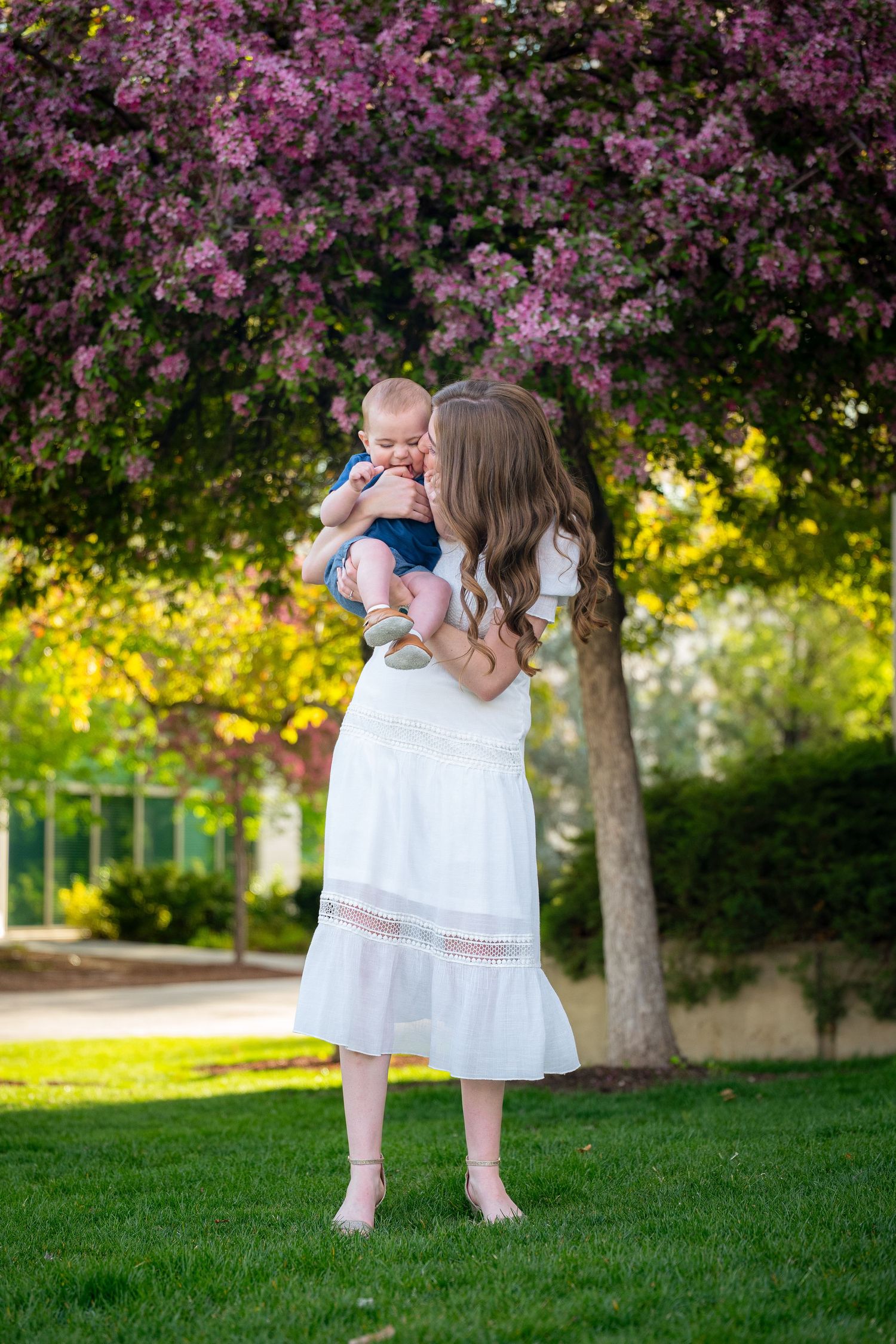 A woman is holding a baby in a garden with blooming flowers.