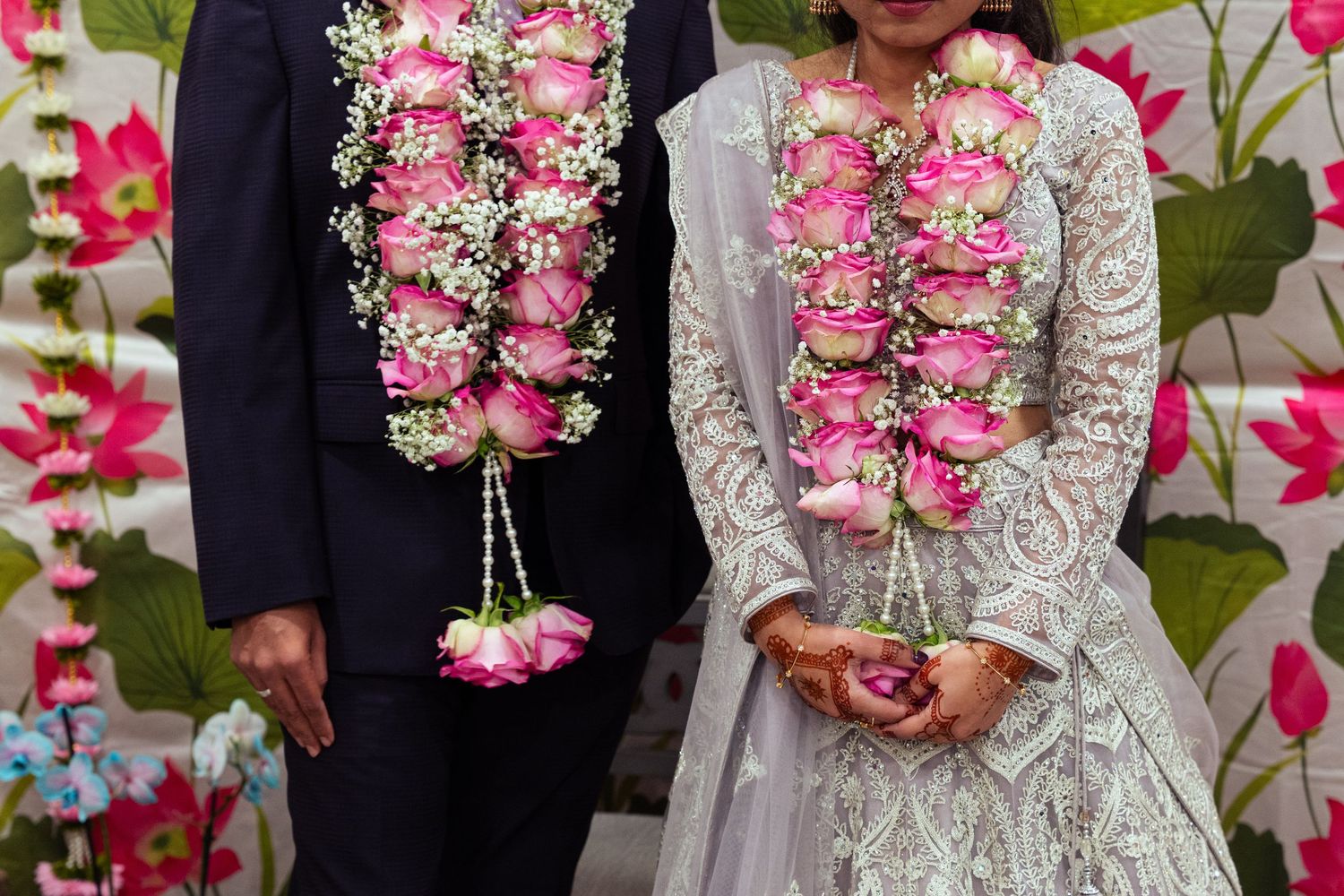 Indian couple in traditional wedding attire exchanging floral garlands of pink roses at a Hindu marriage ceremony.