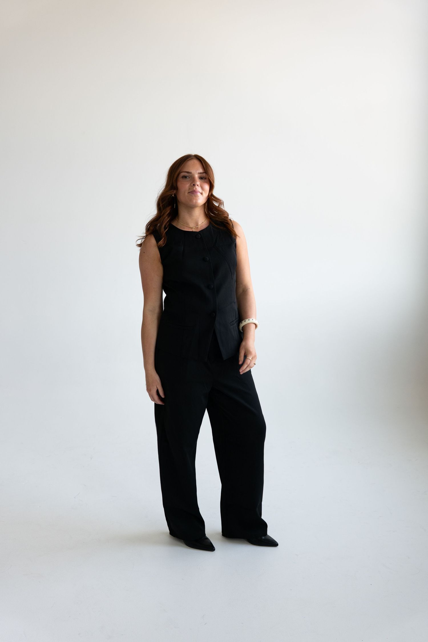 Woman wearing black sleeveless jumpsuit with wide-leg pants standing against white background.