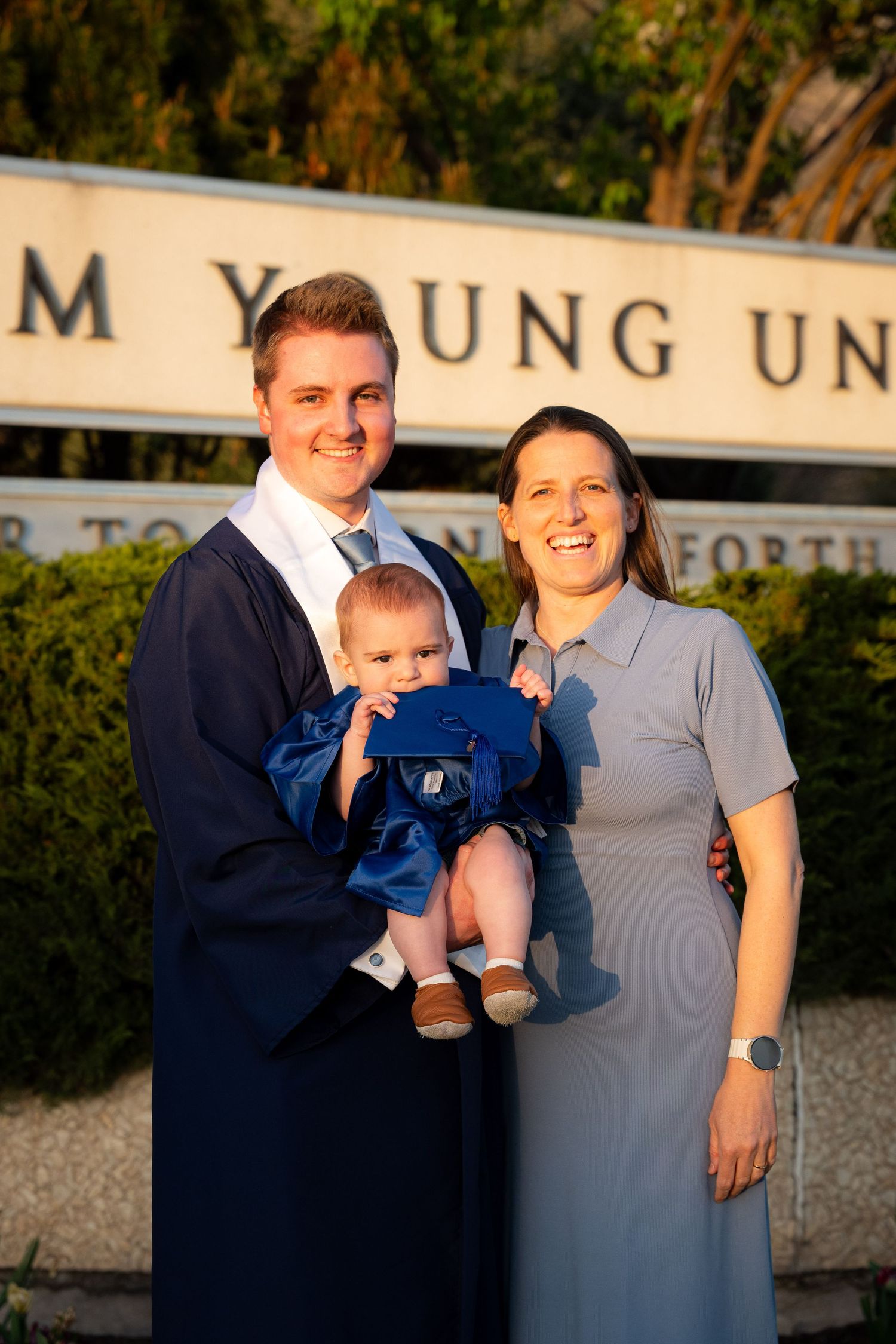 A family, including a couple and a young child, stand together in front of a university sign.