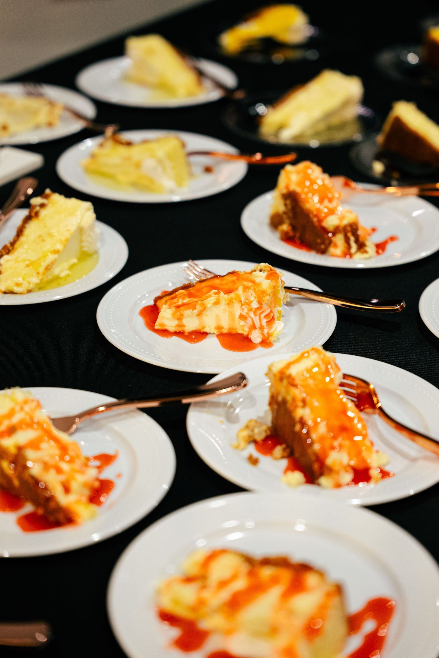 Wedding dessert table with slices of cheesecake topped with strawberry sauce on white plates.
