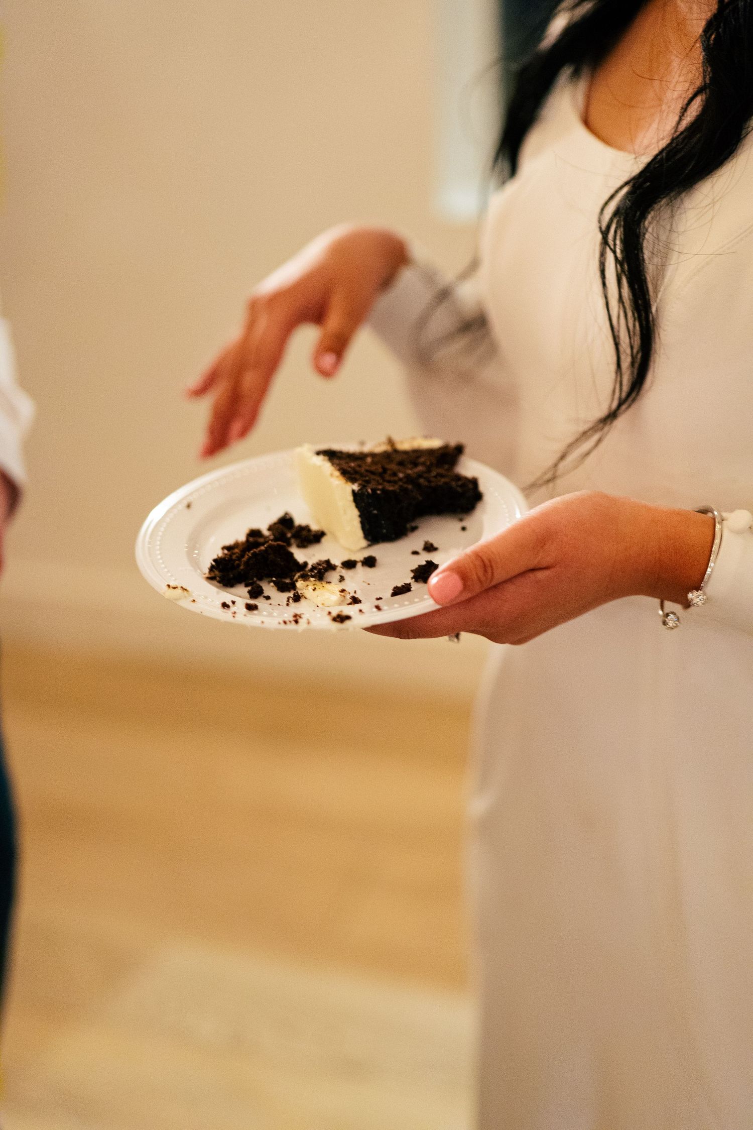 Bride in white dress holding a plate with a slice of dark chocolate wedding cake.