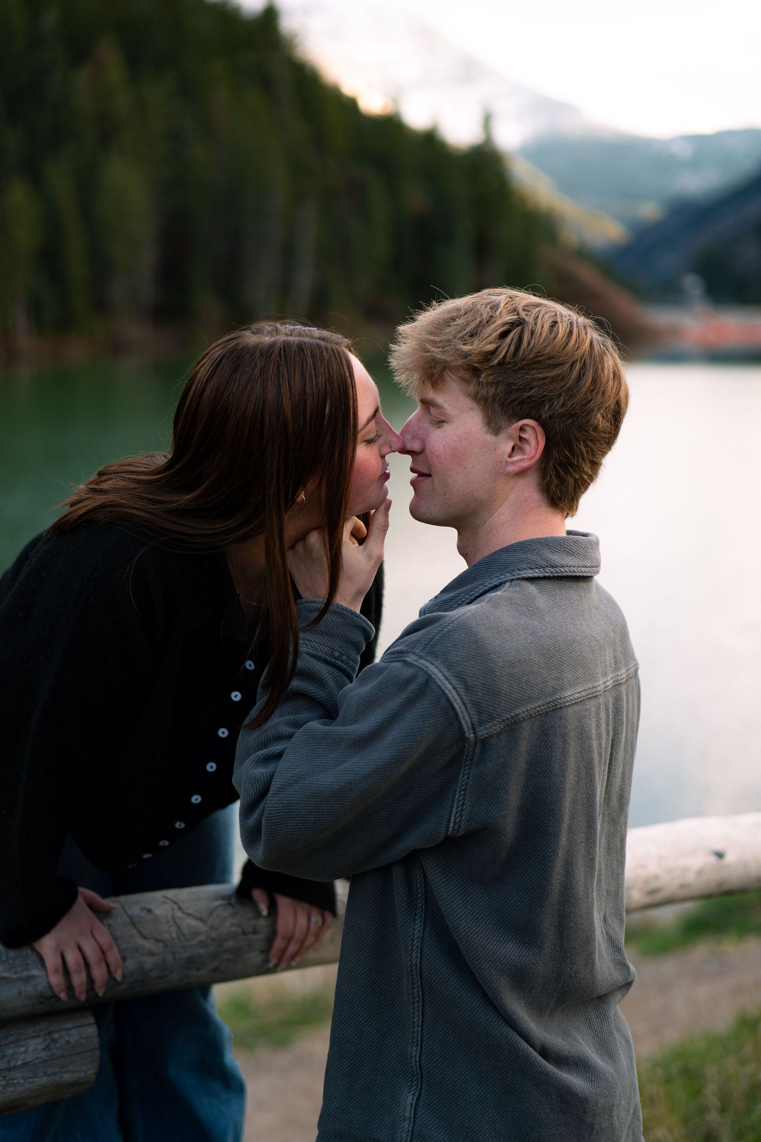 Young couple sharing a romantic moment by a scenic mountain lake surrounded by evergreen forests.