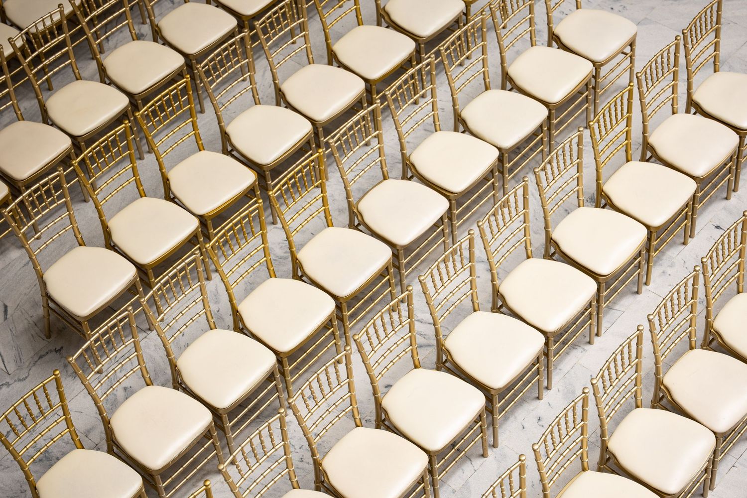 Rows of elegant gold Chiavari chairs with cream cushions arranged in neat rows for a formal event or wedding ceremony.