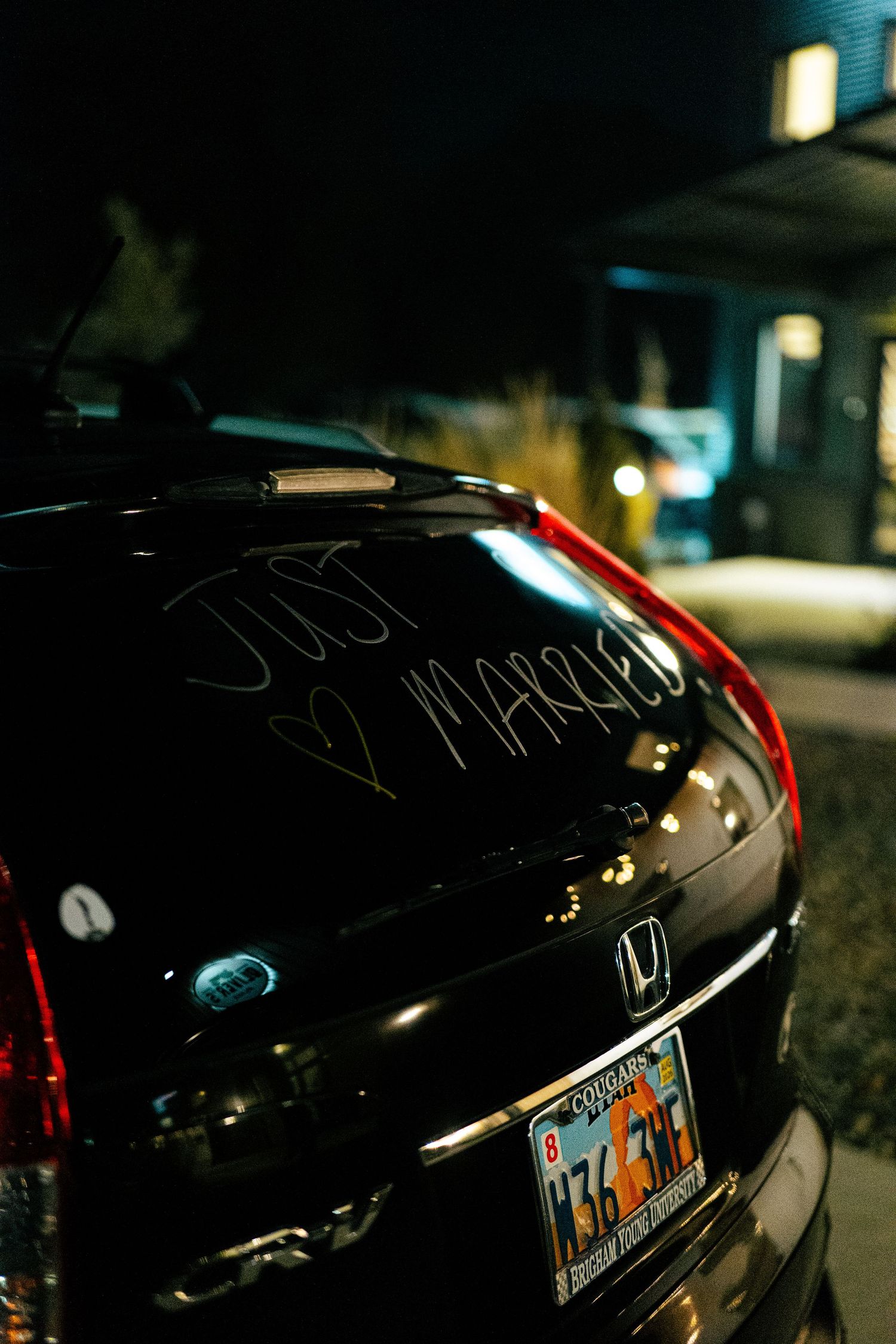 Black Honda car with Just Married written on rear window parked outside at night.
