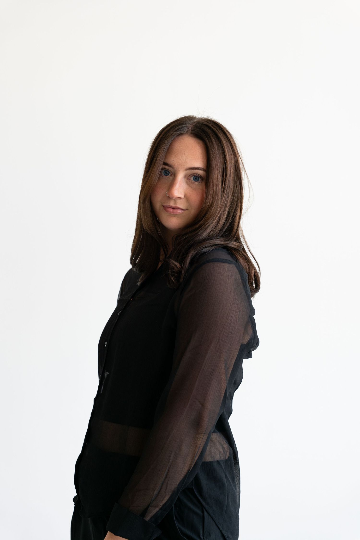 Brunette woman in sheer black ruffled blouse posing with a subtle over-the-shoulder glance in studio.