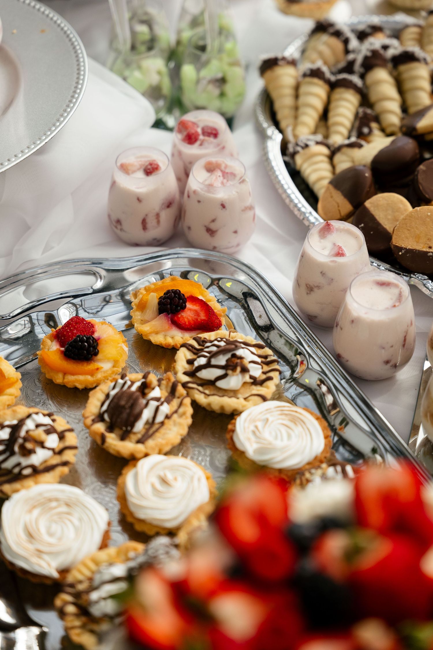 Elegant dessert table with mini tarts, cream-topped pastries, berry parfaits, and chocolate-dipped cannoli at a catered event.