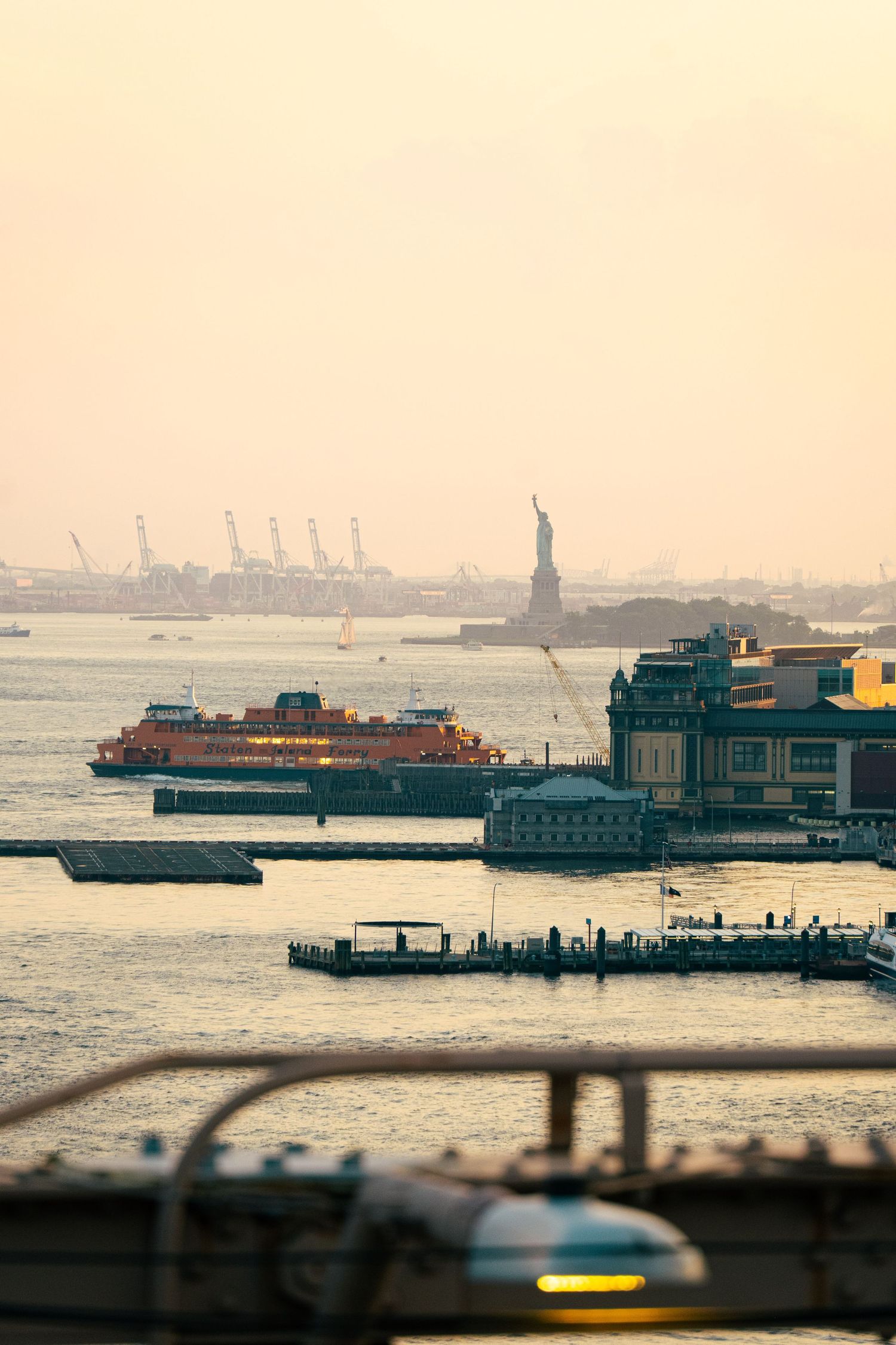 A cityscape with the Statue of Liberty visible in the distance, surrounded by ships and boats in the harbor.