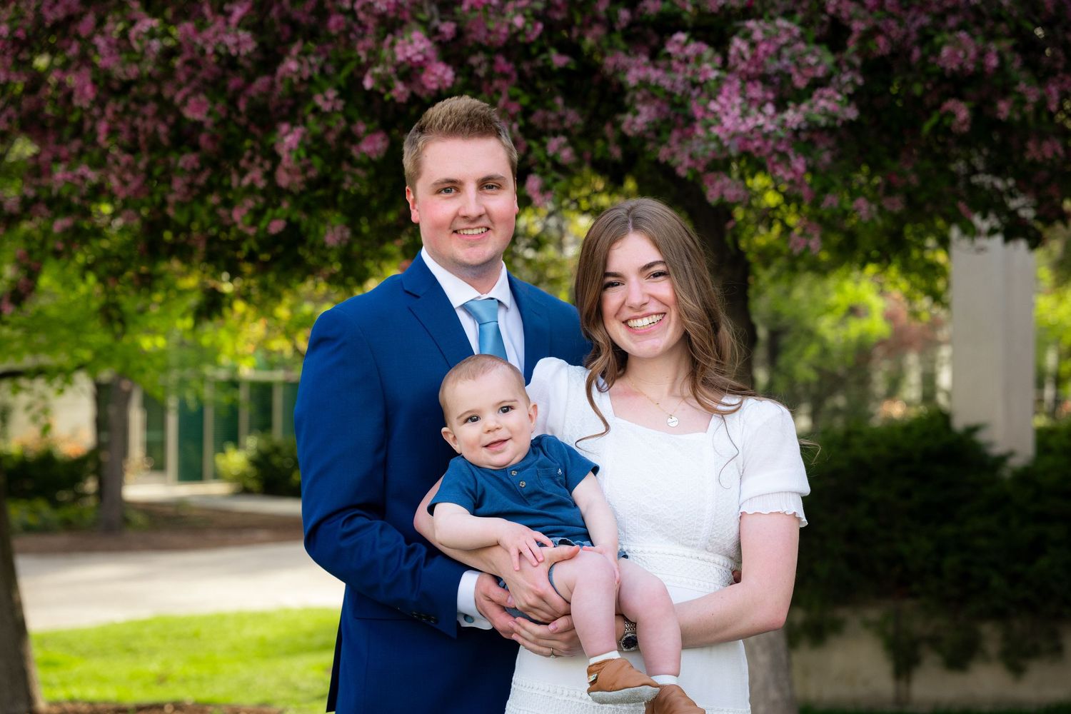 A happy family portrait of a couple and their young baby in a scenic outdoor setting.