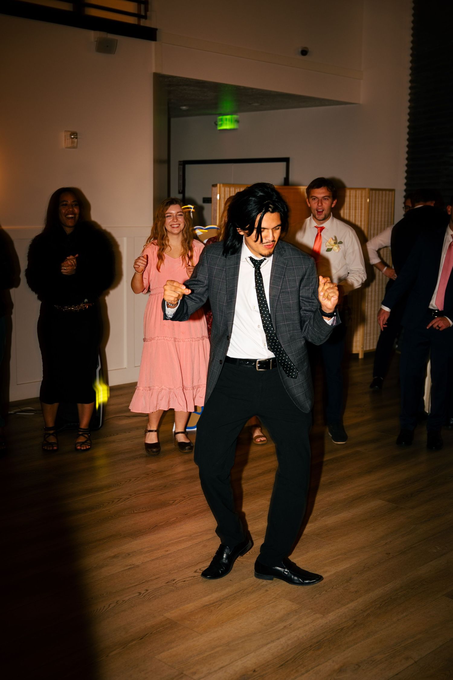 Guest energetically dances at a wedding reception while others celebrate in the background.
